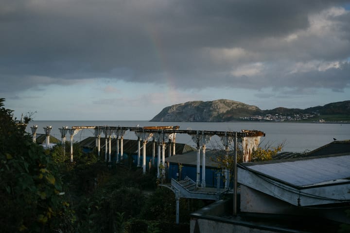 A rainbow arcs onto a large hill on the edge of Llandudno bay. In the foreground a building lies in ruin.