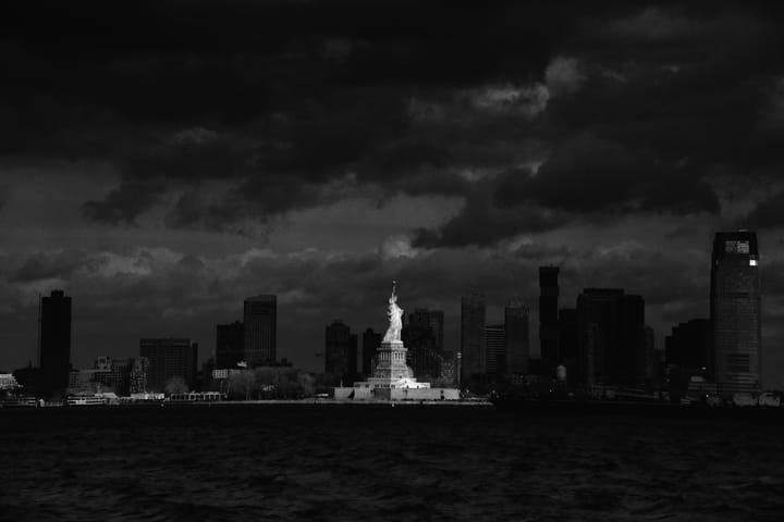 The Statue of Liberty stands bright against a darker Manhattan skyline.