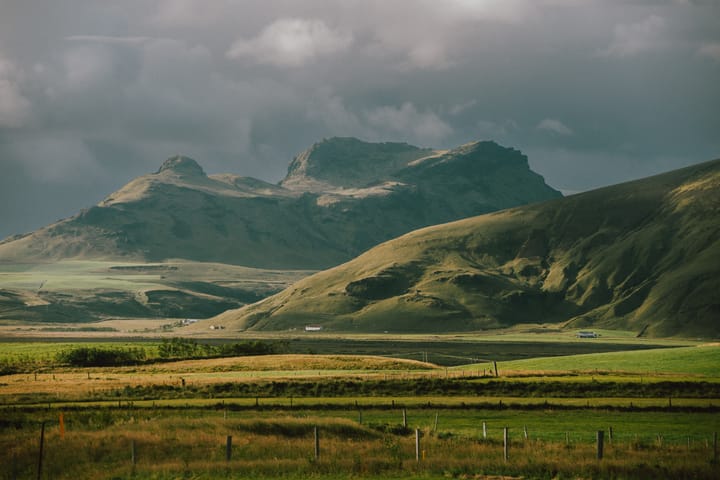 Lucious green fields extend across a mountain range on an overcast day.