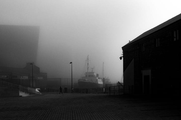 A person walks past a ship in a dry dock on a foggy day.