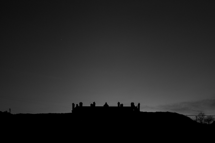 Moody black and white landscape with a large Victorian house on the top.