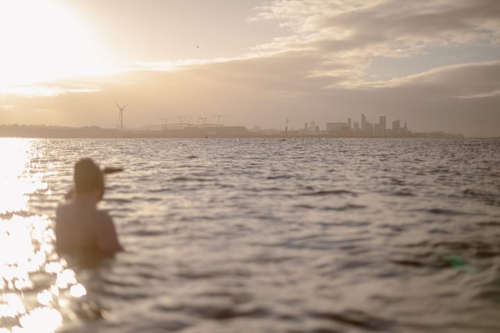 A swimmer at sunrise looks towards Liverpool on the horizon.