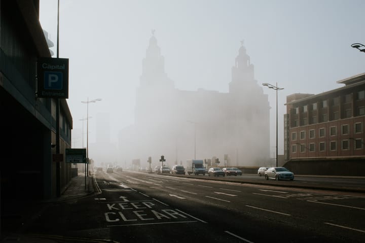 Fog causes the Liver Building to appear hazy as traffic passes by it.