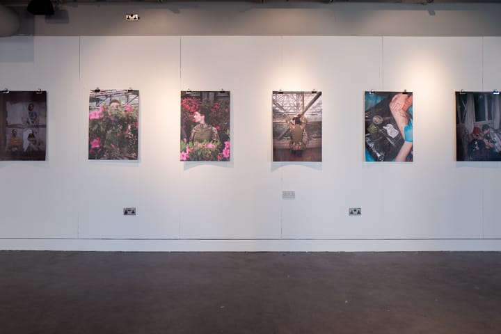 On a gallery wall, there are photos of pink flowers and a woman in military gear behind them.