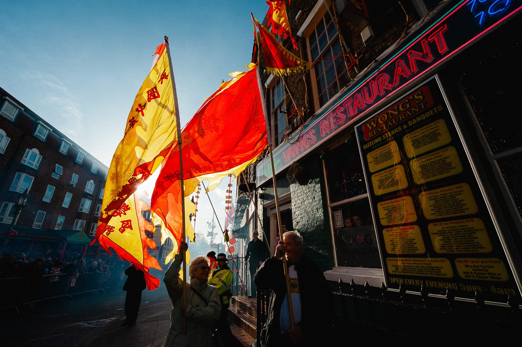 People carrying flags are backlit by the sun. The colour of the flags jumps out against the darker background.