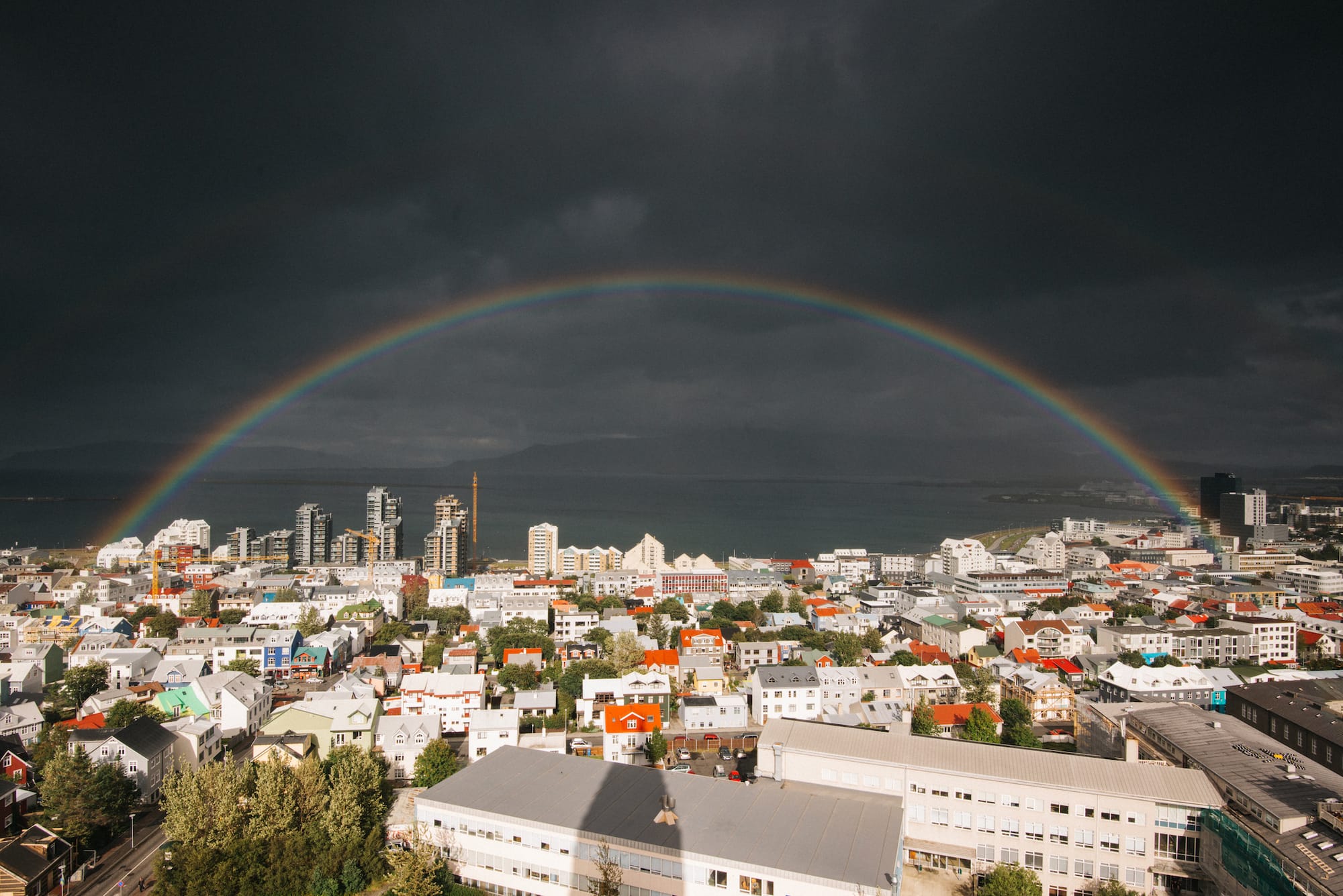 The view from the top of the Hallgrímskirkja church. There is a strong double rainbow and a view across the bay to mountains in the distance.