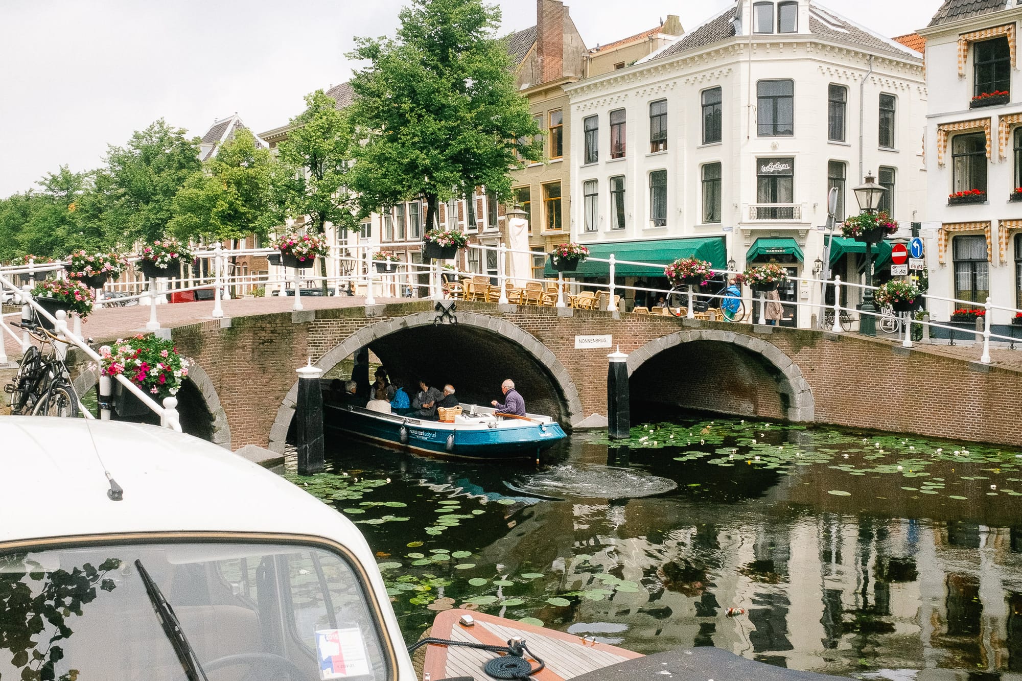 A barge sails underneath a bridge in Leiden, Netherlands. There are flower baskets along the bridge.