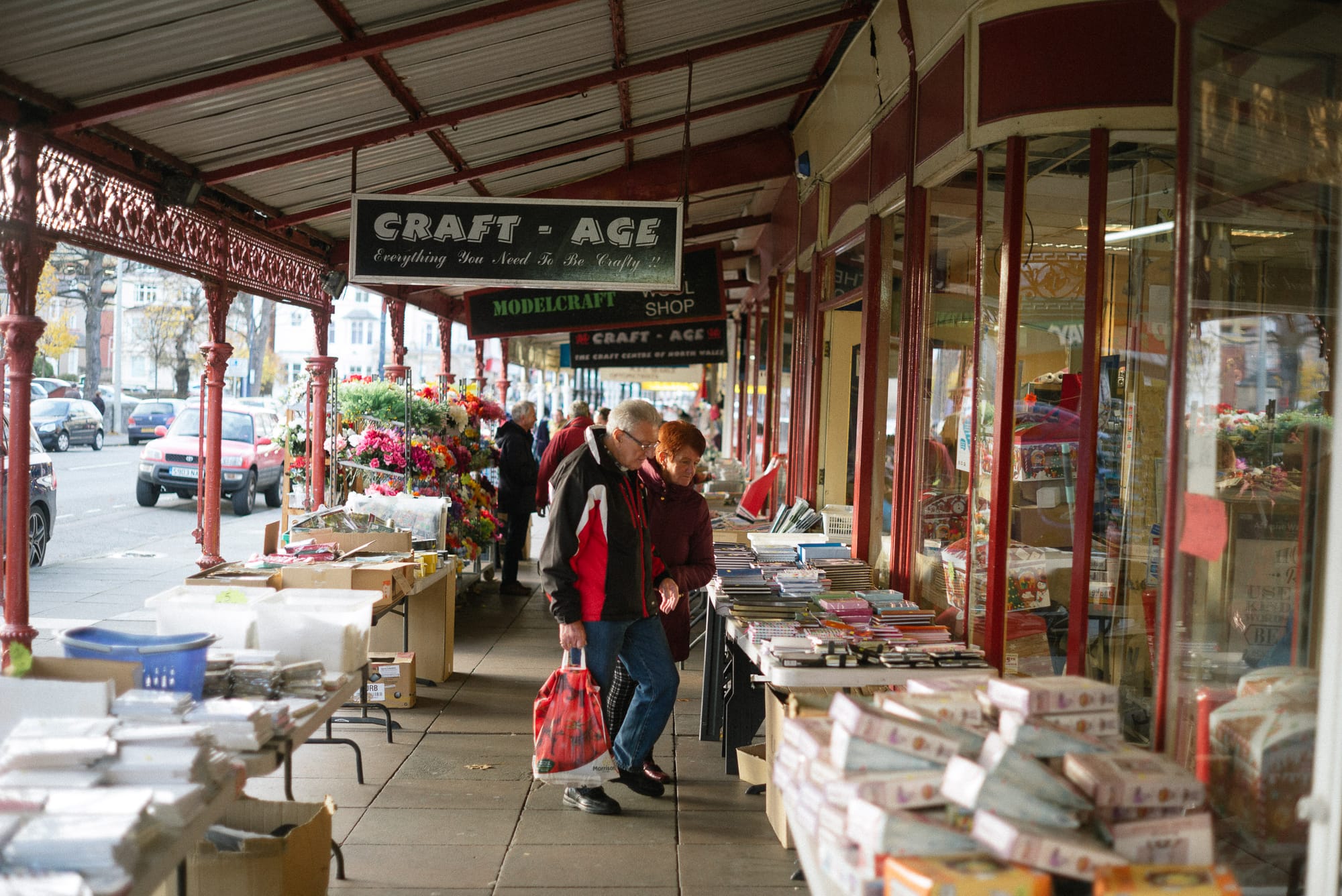 An old couple browse books in a sheltered street arcade.