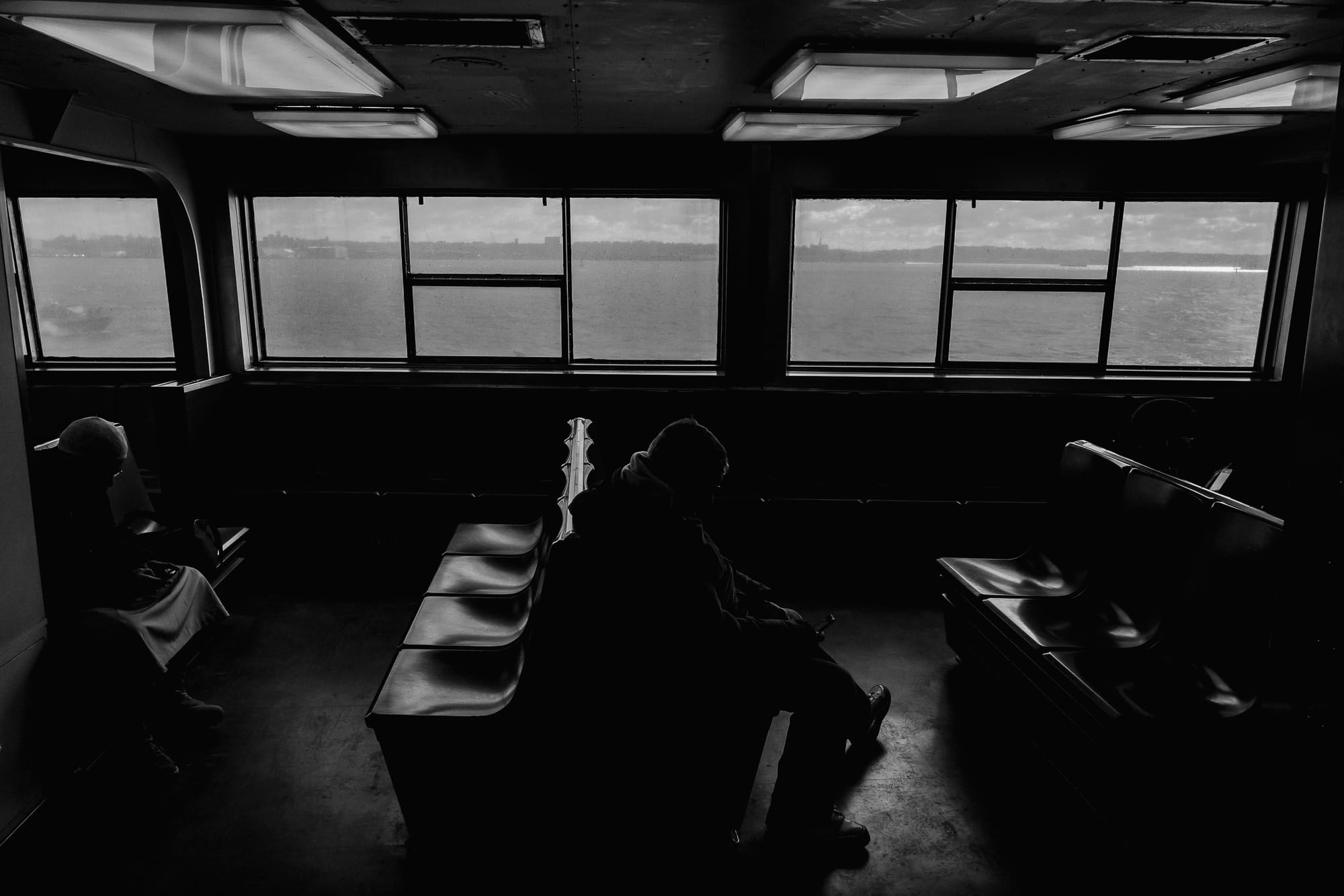 A couple of people sit on the Staten Island ferry as it crosses the Hudson River. It’s a bit bleak.