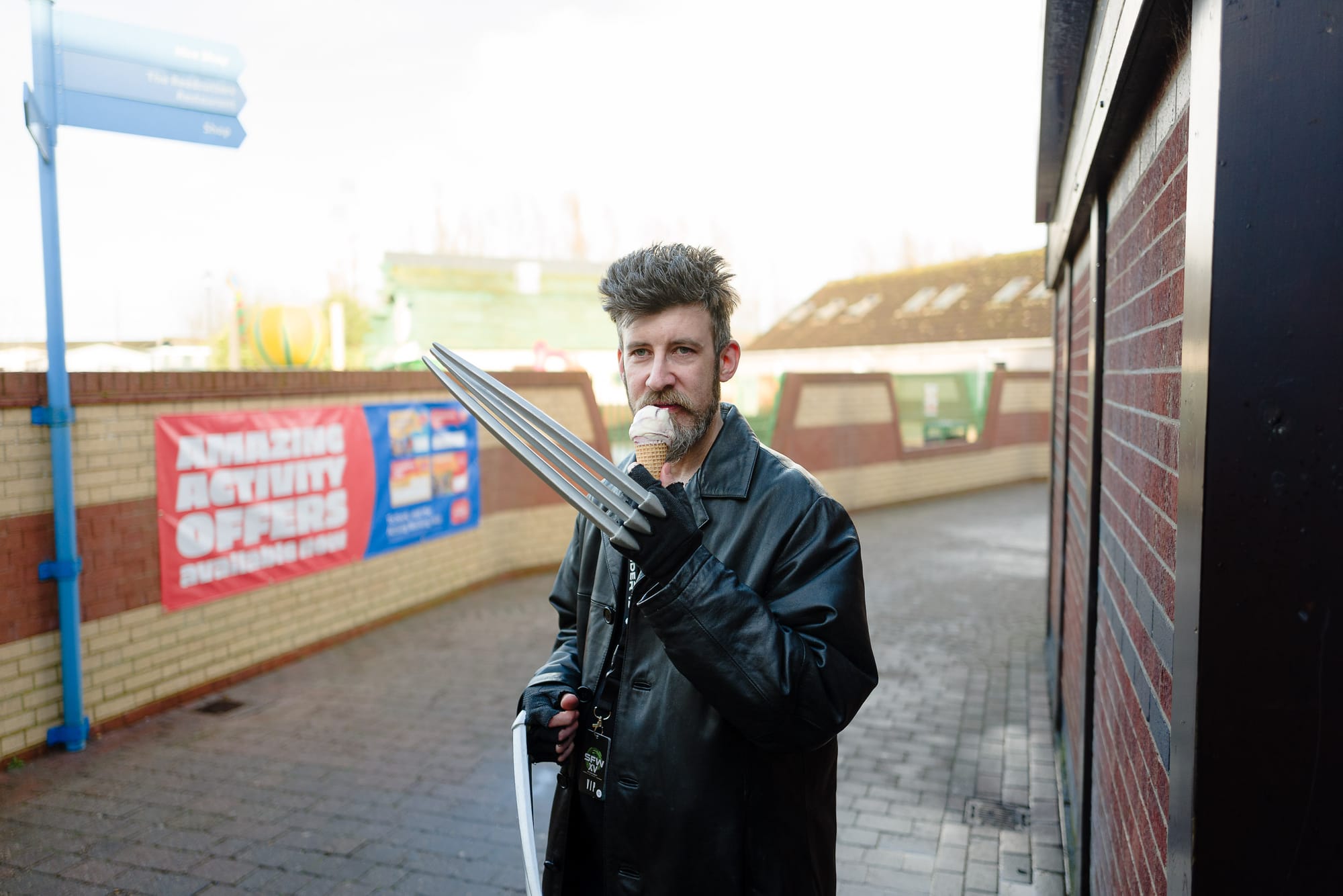 A man dressed as Wolverine with his claws out enjoys an ice-cream at a holiday park.