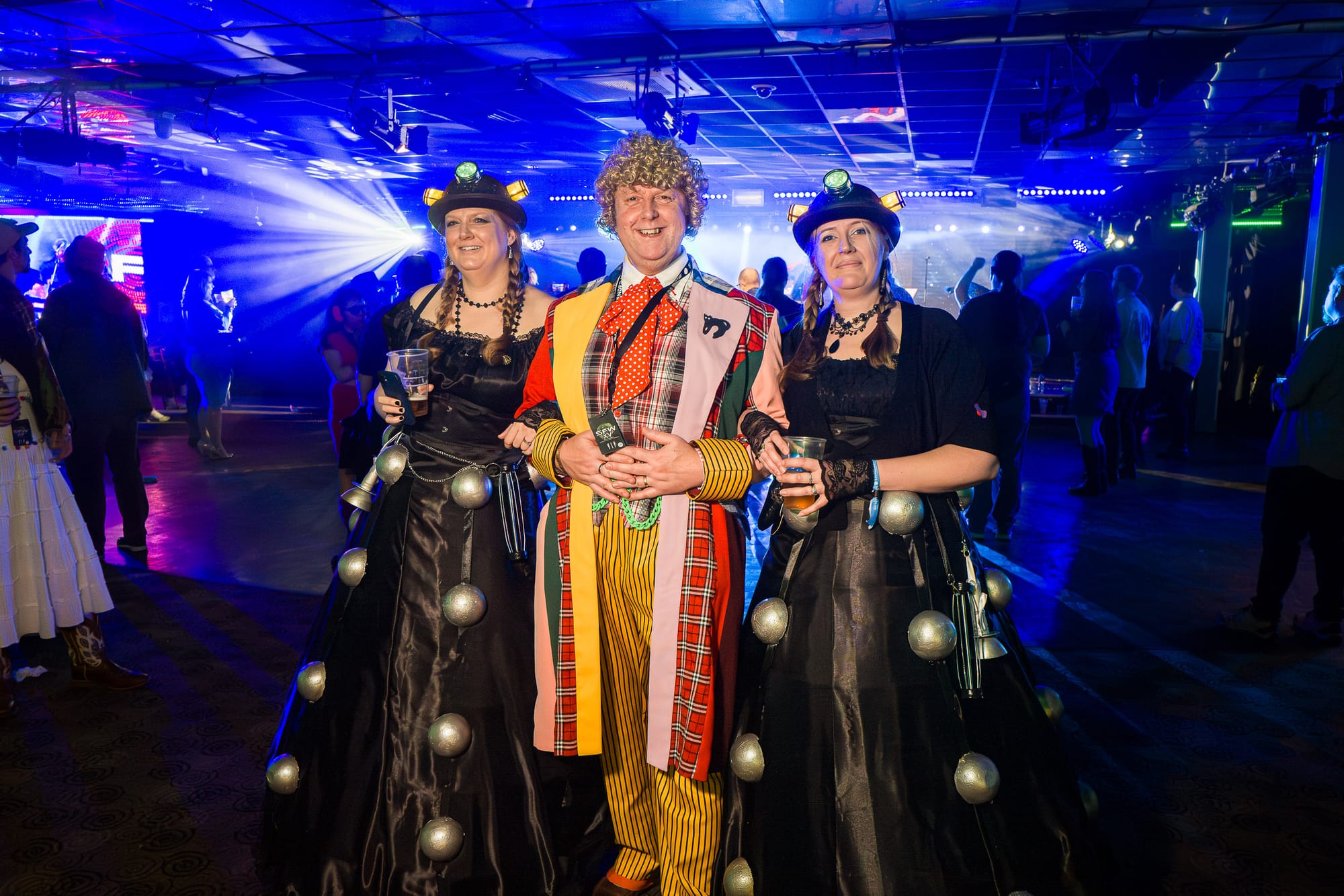 A man dressed as Colin Baker’s Doctor poses with two women’s dressed in Dalek themed dresses.