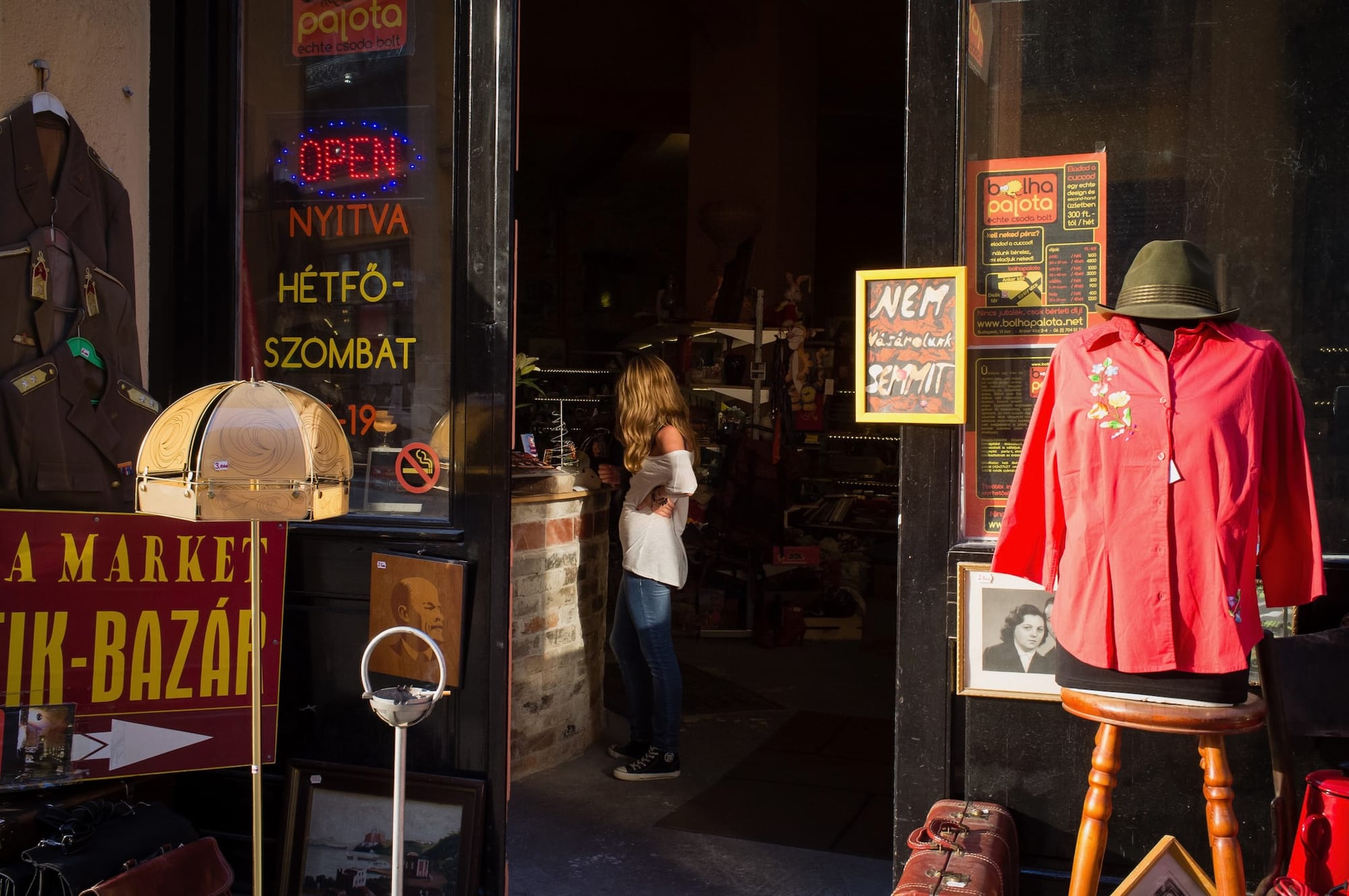 A woman, perfectly lit by the sun, stands in a shop doorway.