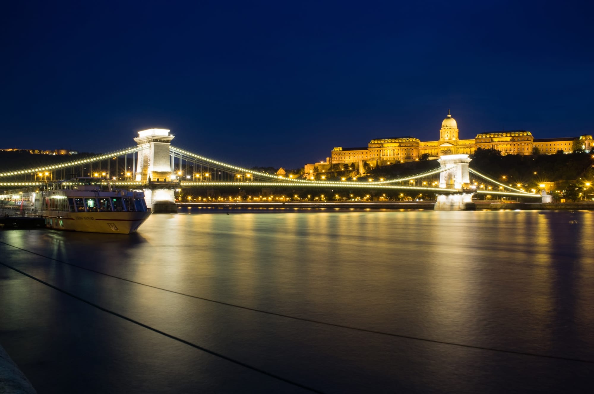 The main bridge in Budapest lit up white at dusk.
