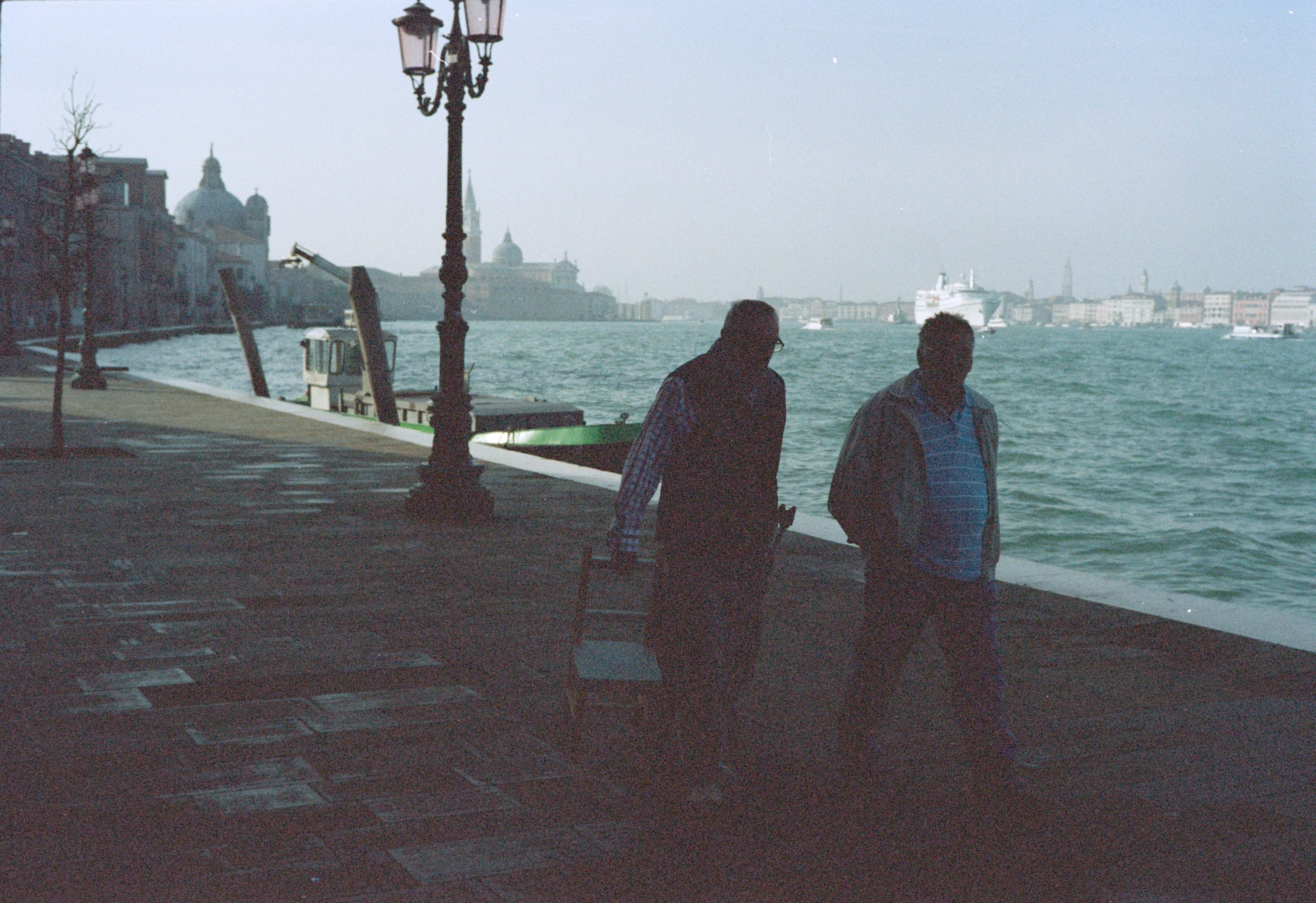 A couple of men drag some chairs along a street in Venice next to a canal.