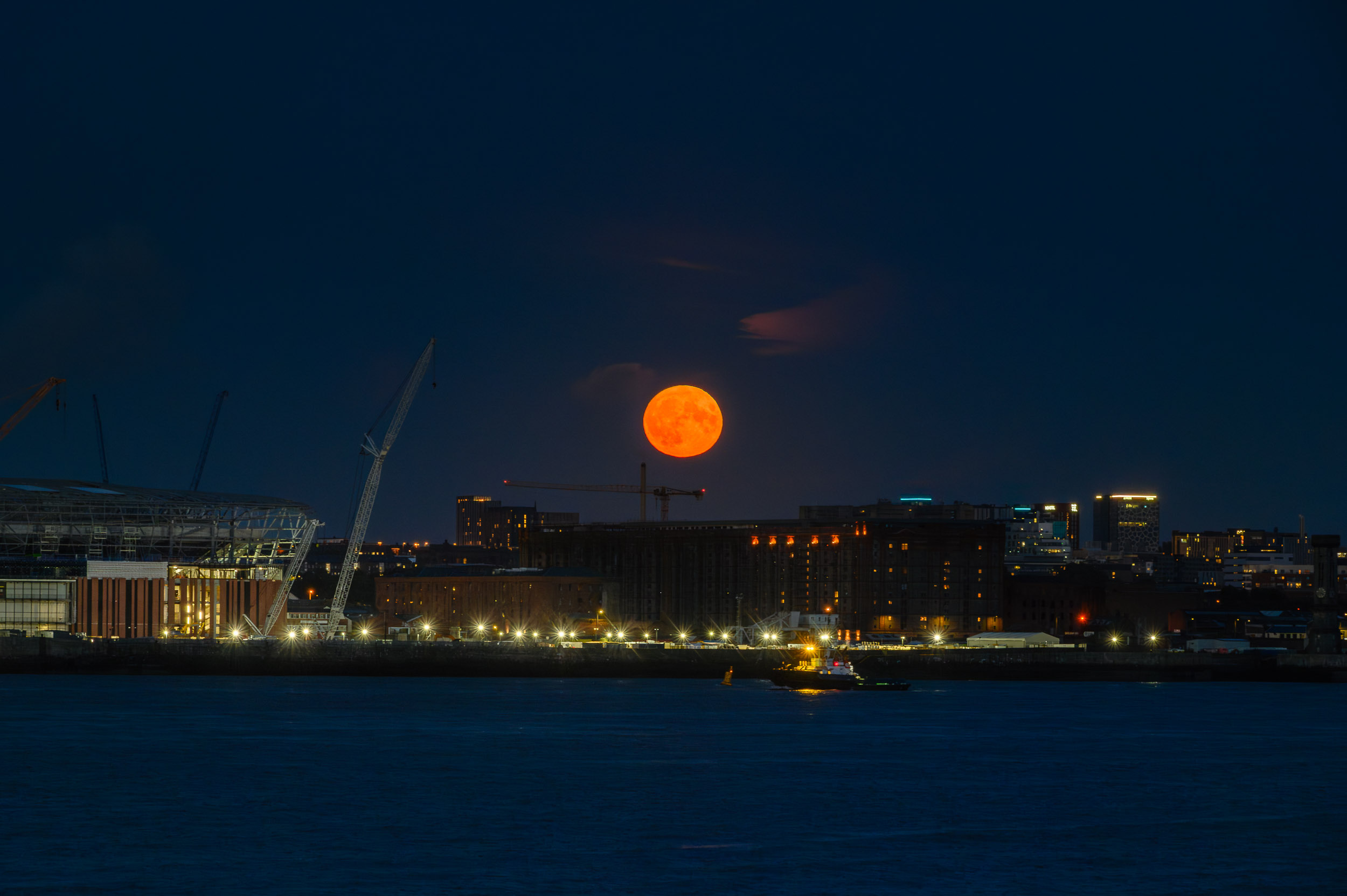 Super blue moon rises through the clouds over the Liverpool waterfront. A tug sails down river.