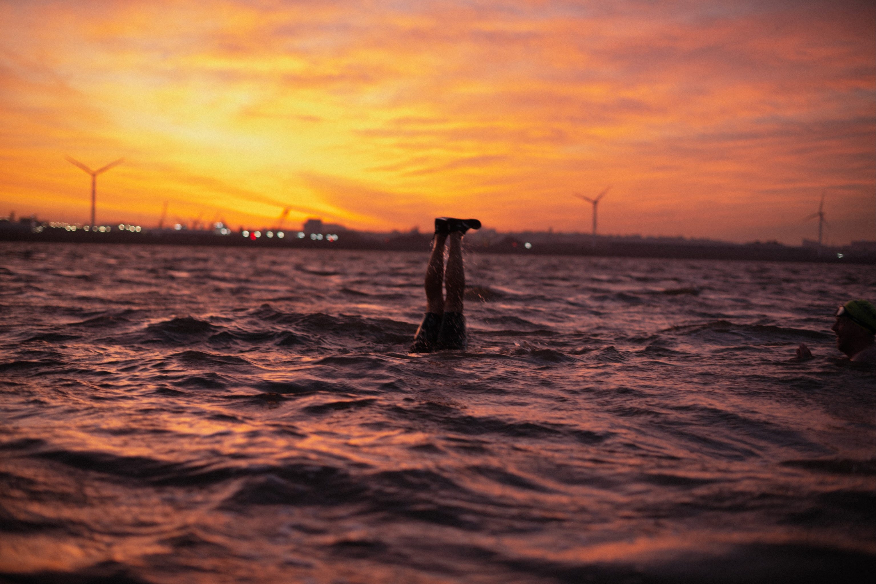 A man does a handstand in the River Mersey at sunrise. Only his legs are visible.