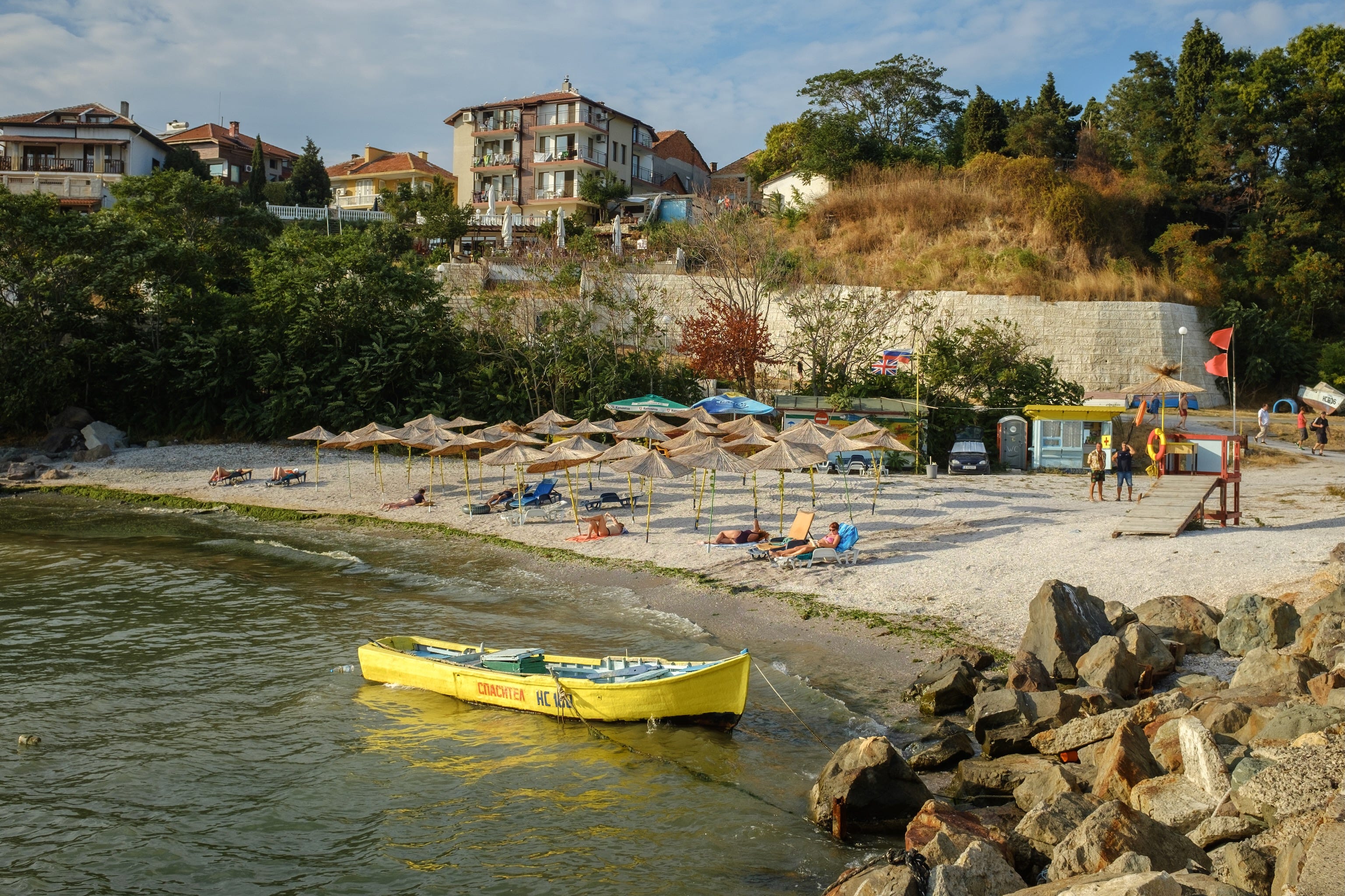 A beach in Nessebar. There's a yellow boat moored by some rocks, and lots of beach umbrellas out.