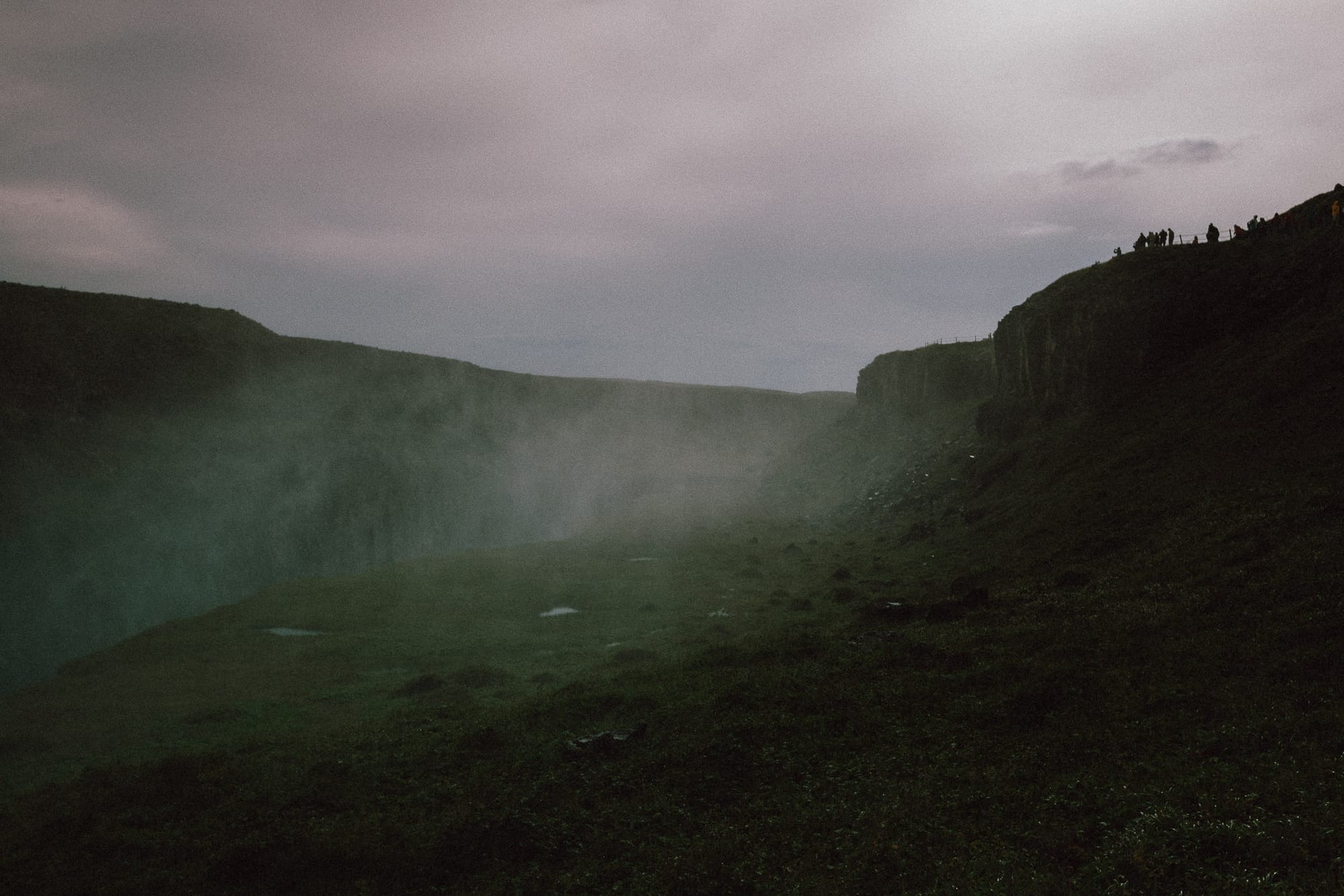 Mist rises from a gorge by a watefall as people on the clifftop watch.