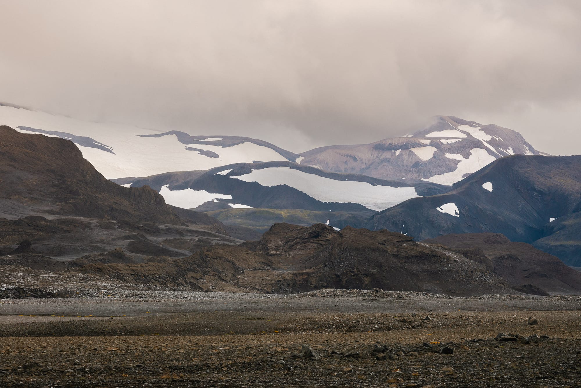 A few small islands in a lake in Iceland with mountains in the distance. As the sun sets rays of stream through the clouds.