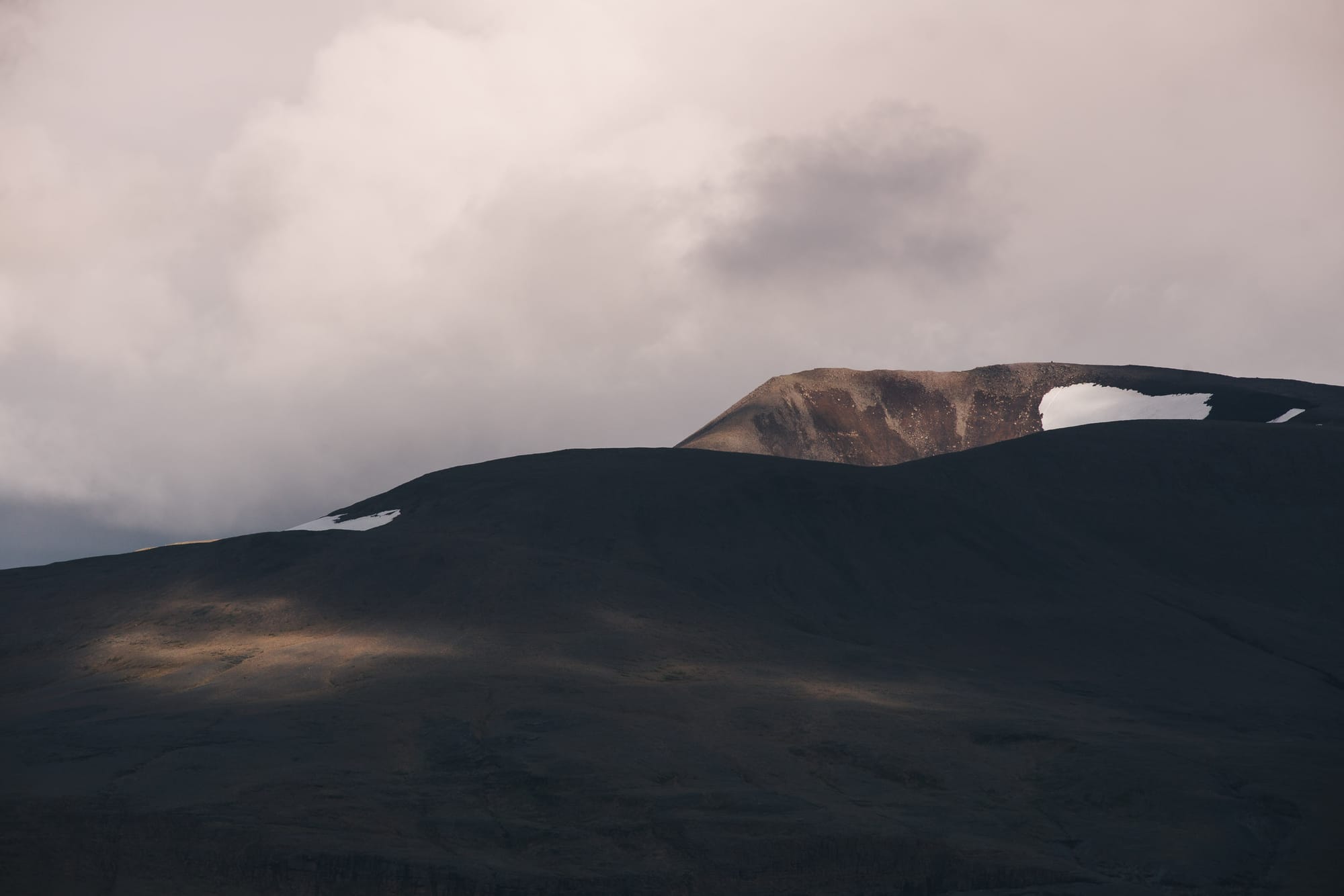 Sunlight moves over a mountain with patches of snow on.