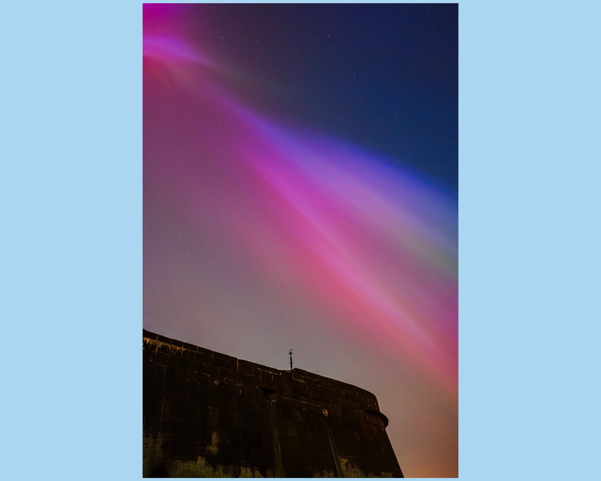 Purple and blue bands of light streak across the nights sky above an old fort.