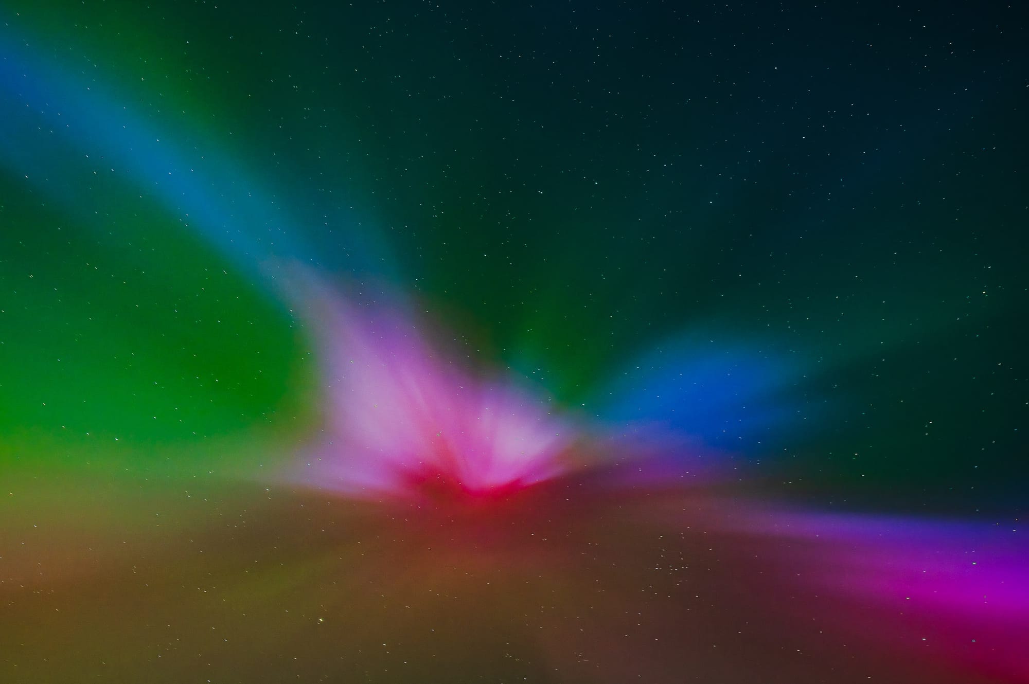 A rainbow like aurora fills the sky against a backdrop of stars.