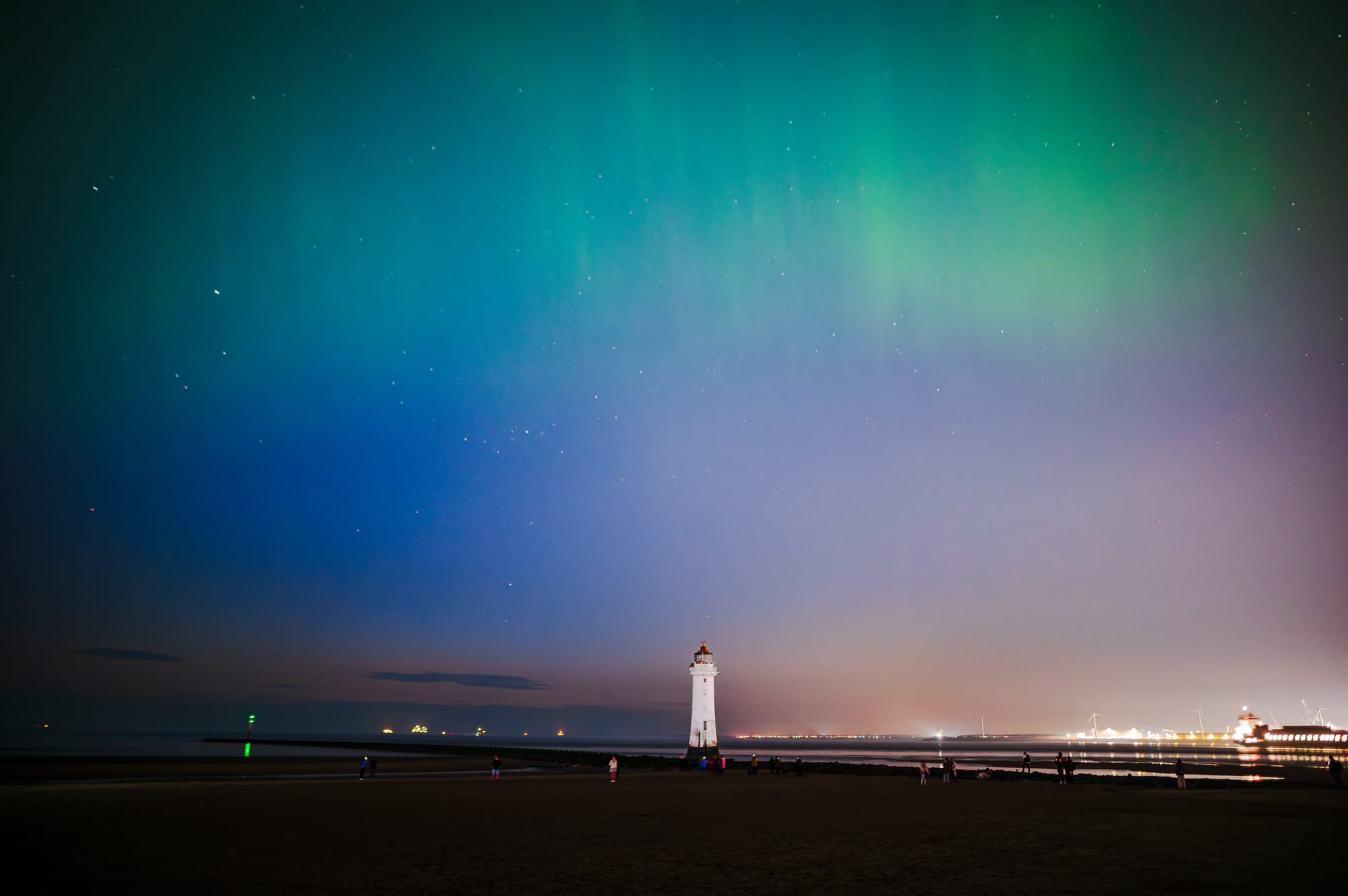 A green aurora flies above New Brighton lighthouse as people gather to watch.