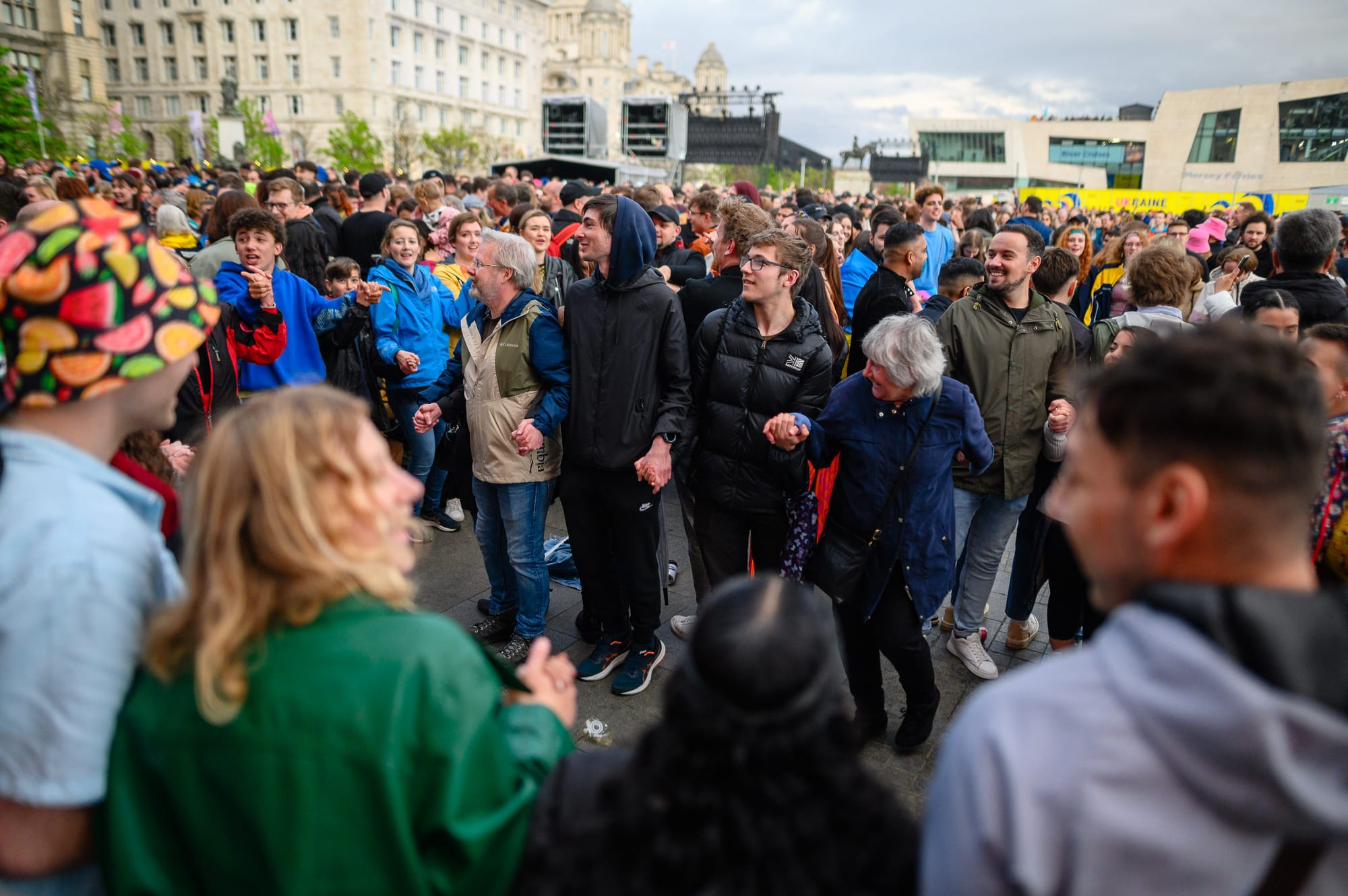 Members of the audience at an outdoor live music event hold hands and dance together.