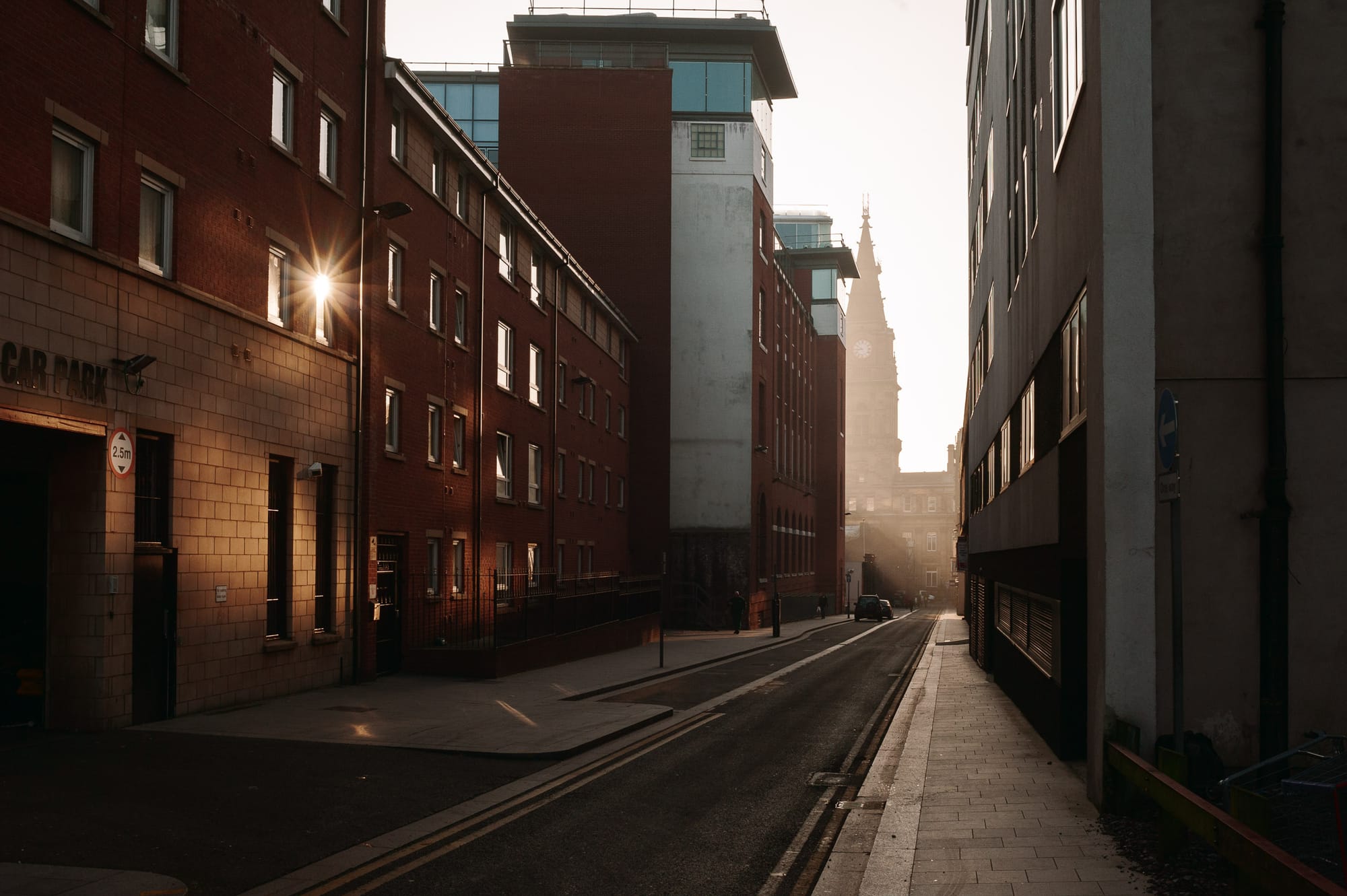 A side street in Liverpool. At the end of the street is a building shrouded in fog. Sunlight pours down the street bouncing off a single window.