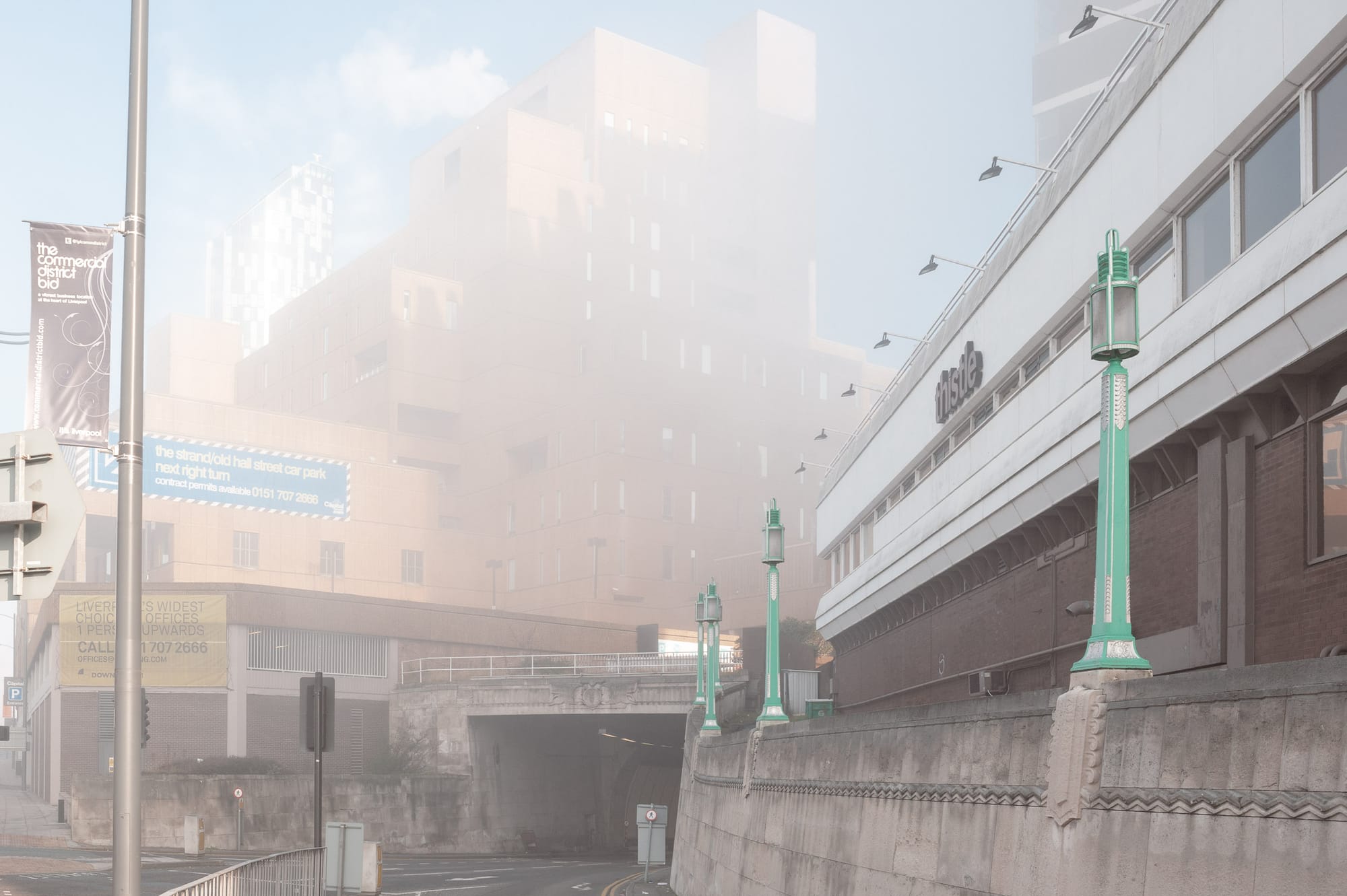 Foggy morning in Liverpool. The orange sandcastle like building is faded in fog. A tall glass skyscraper in the distance shines in the sun.