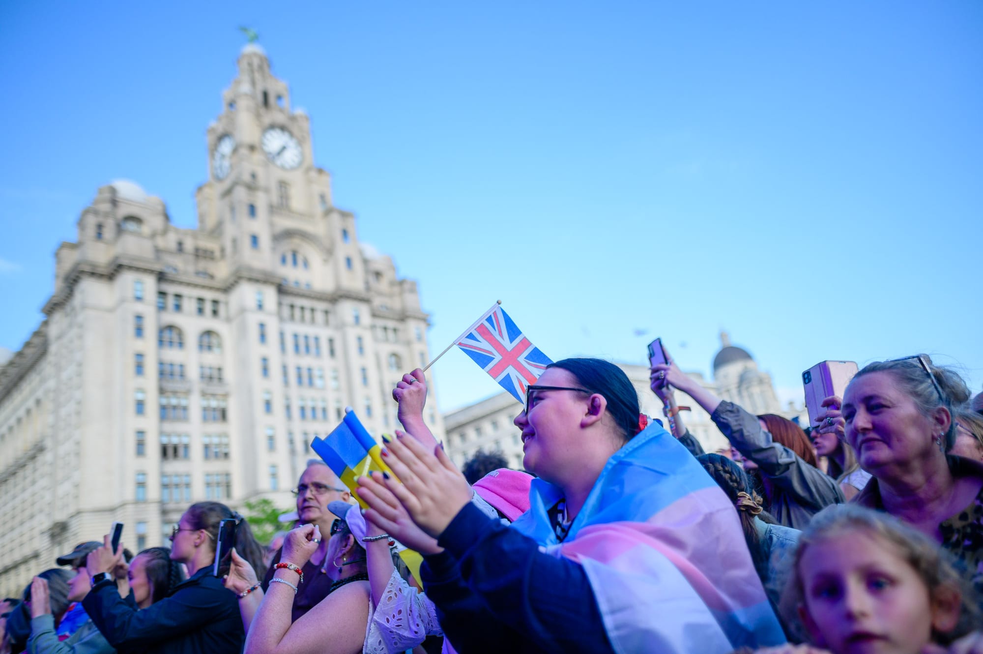 An afternoon on the Liverpool waterfront. There is a gig on and one person has a trans flag draped over them.