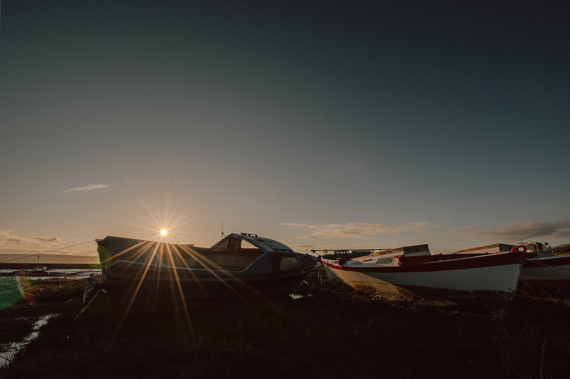 A starry sun sets just above a pair of boats resting on a riverbed.
