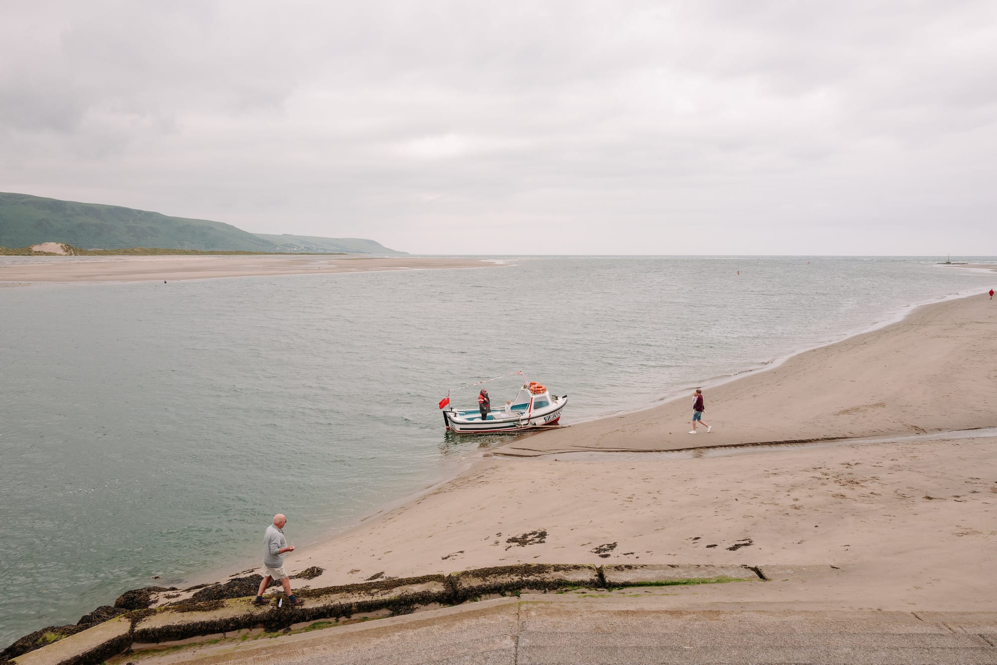 A little boat runs ashore to drop off passengers. On the left are big hills.