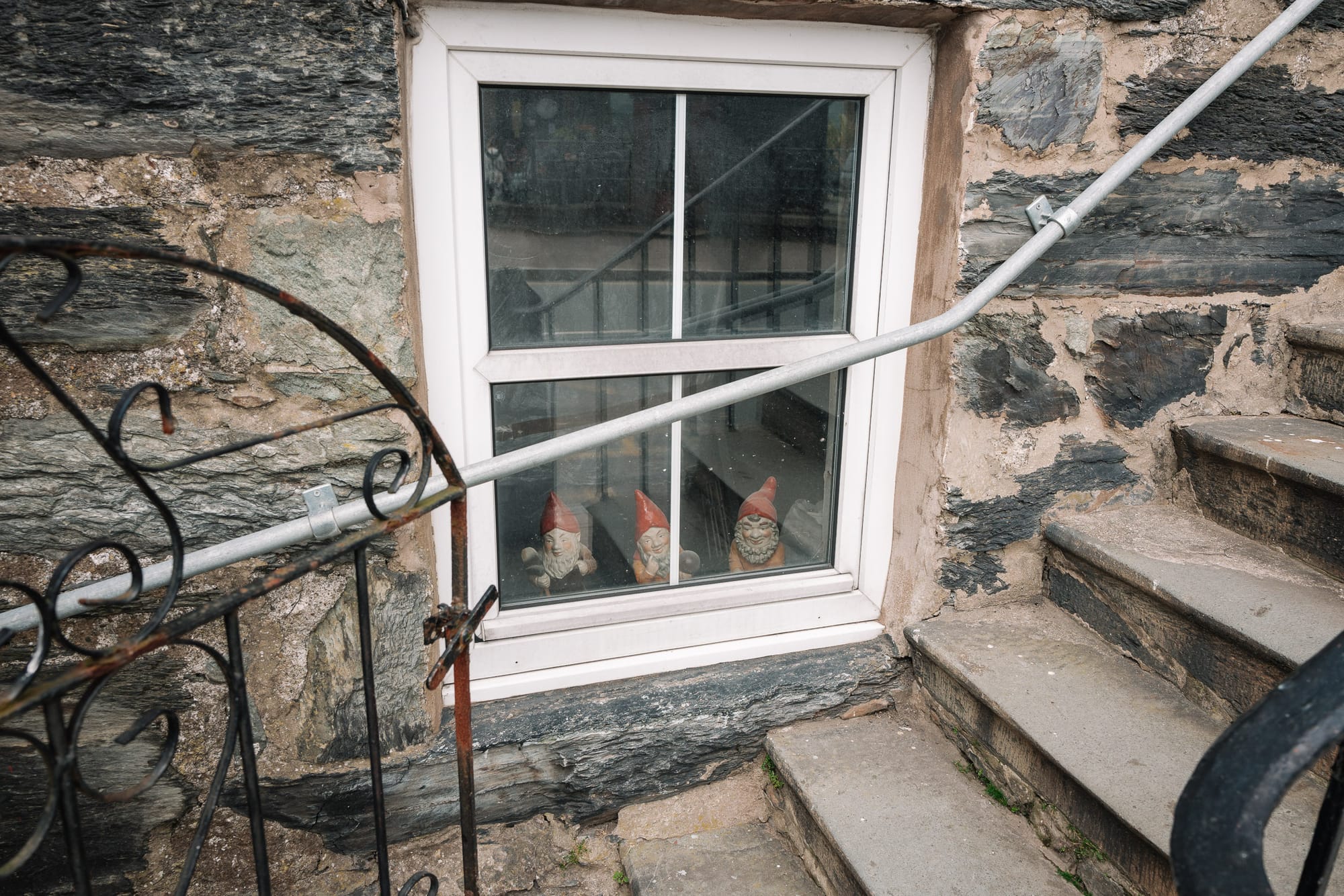 3 little gnomes sit looking out of a window in and old home.