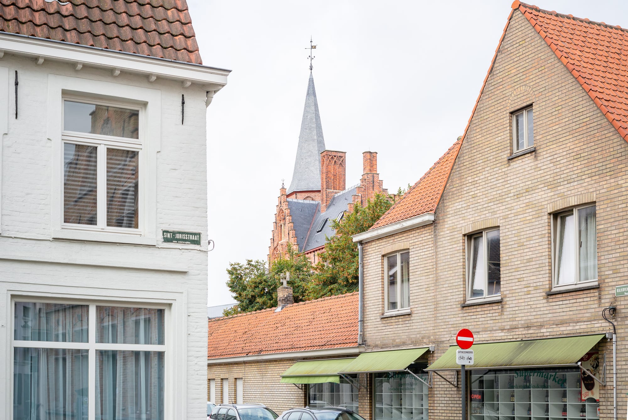 A crop of two homes in Bruges. In between is a beautiful brick roof, and in the distance is a church spire.
