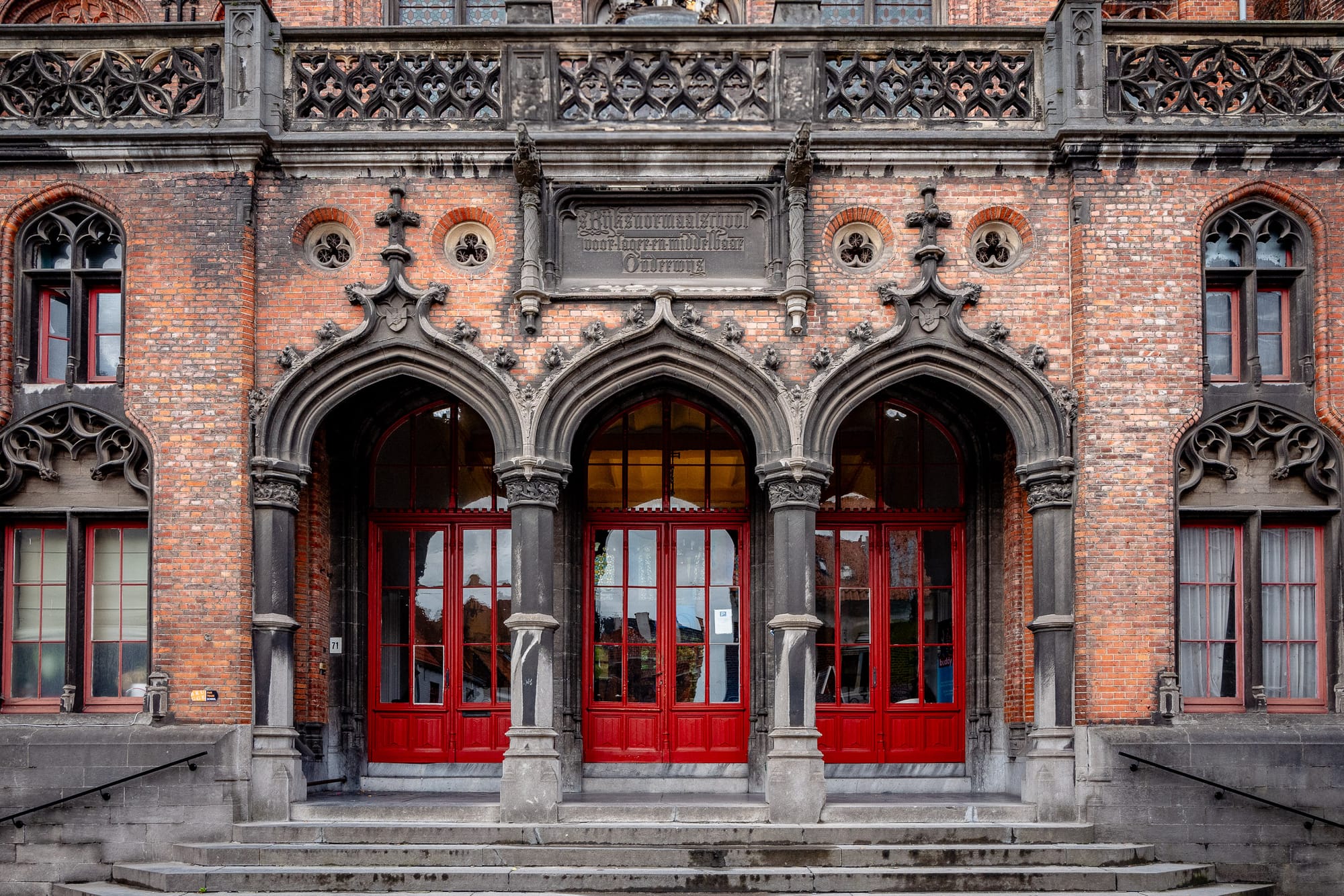 A series of large red doors stand at the entrance to an ornate school building.