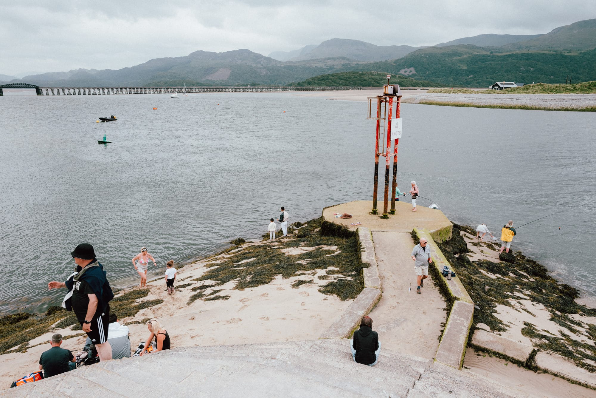 At the end of a tide wall various people are crabbing, fishing, and taking in the view down the estuary.