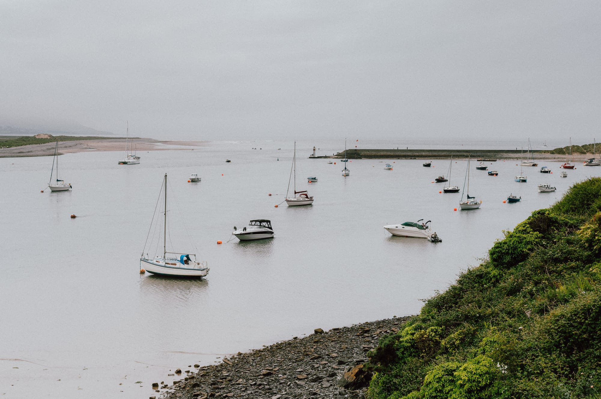 Lots of little boats rest in low water as the tide goes out. It’s overcast.