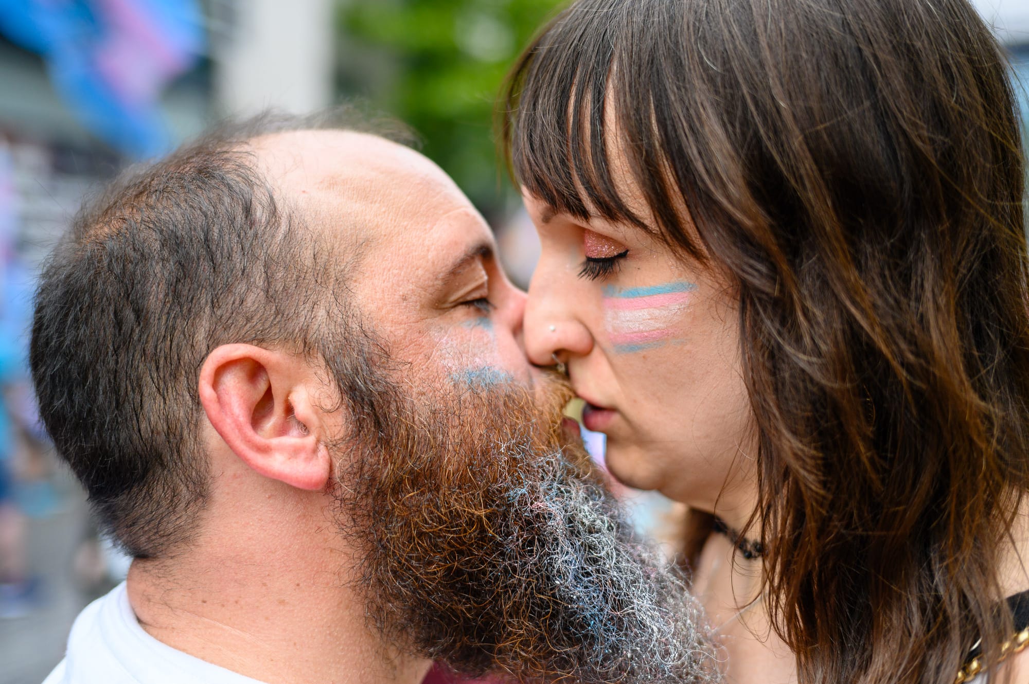 A white couple with trans flags painted on their cheeks kiss.