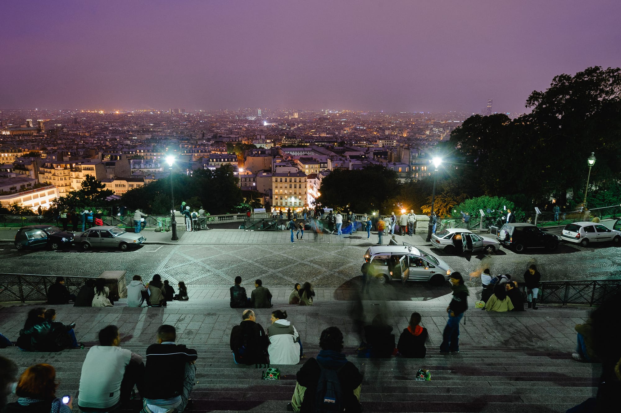 With Sacré-Cœur behind, people sit on the steps and look over the skyline of Paris at dusk.