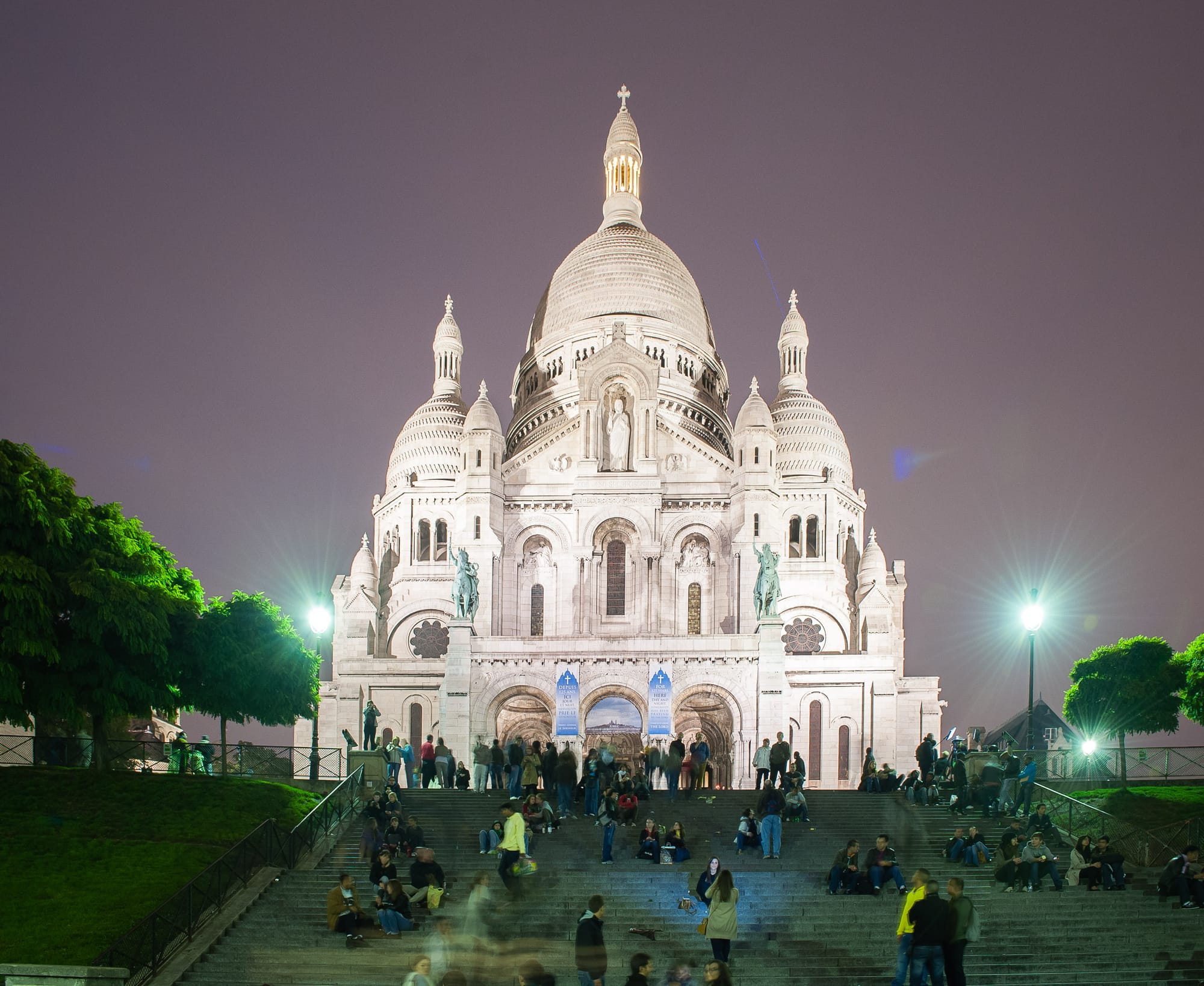 At the top of some steps is the Basilique du Sacré-Cœur. A stunning building all in white that stands tall on top of Montmartre. People sit on the steps below.
