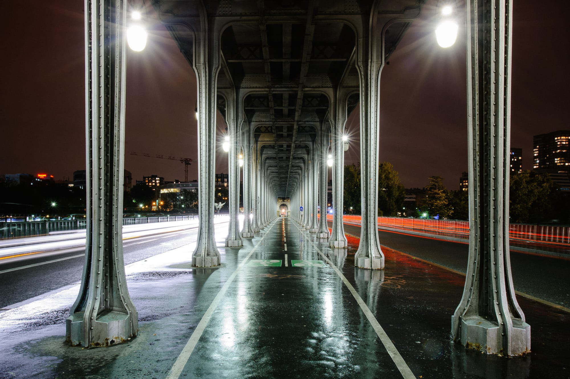 Underneath a railway bridge at night. On either side of the bridge are light trails from passing cars.