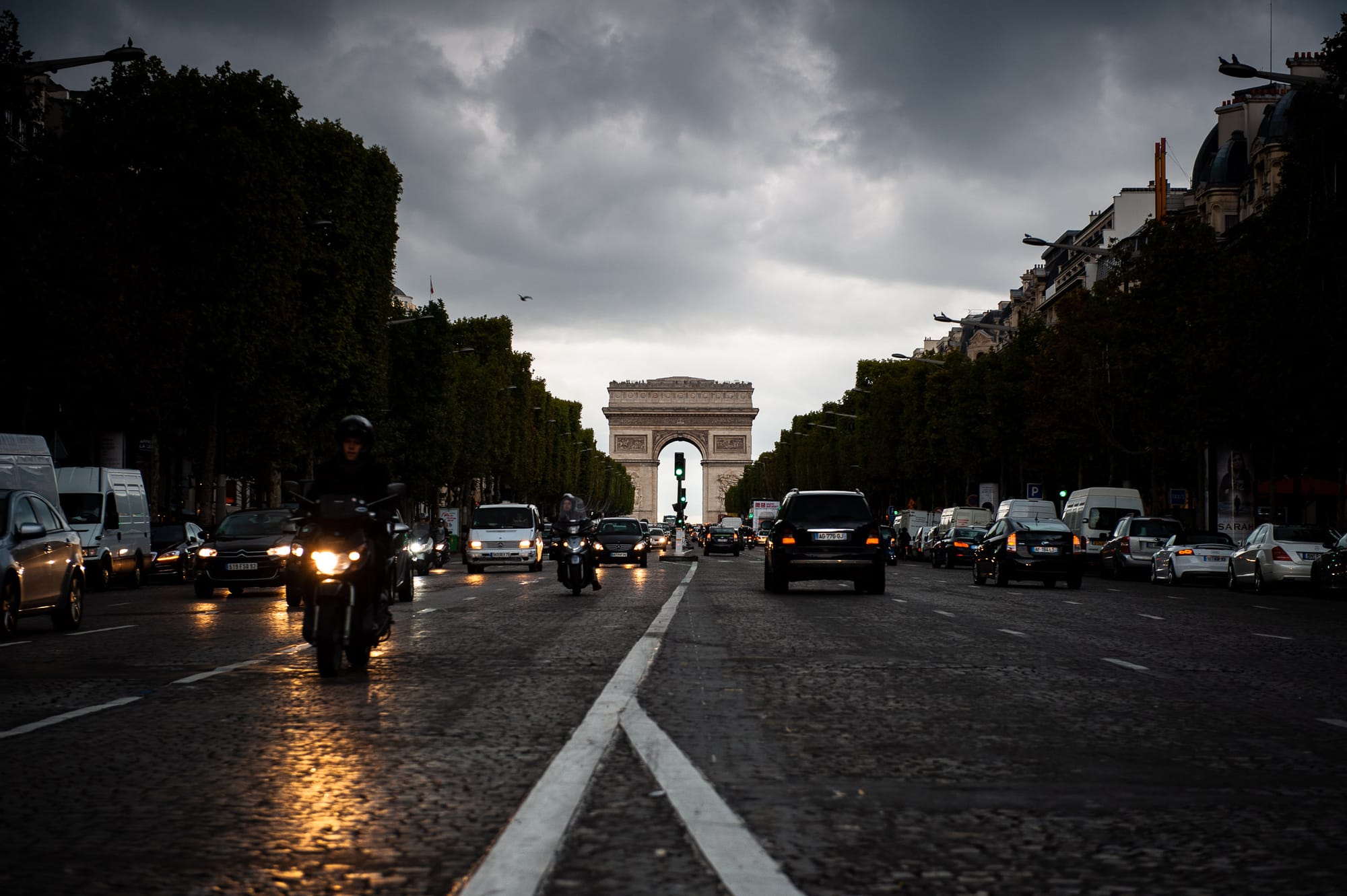 A view down the Avenue des Champs-Élysées towards the Arc de Triomphe with traffic passing either side of the photographer.