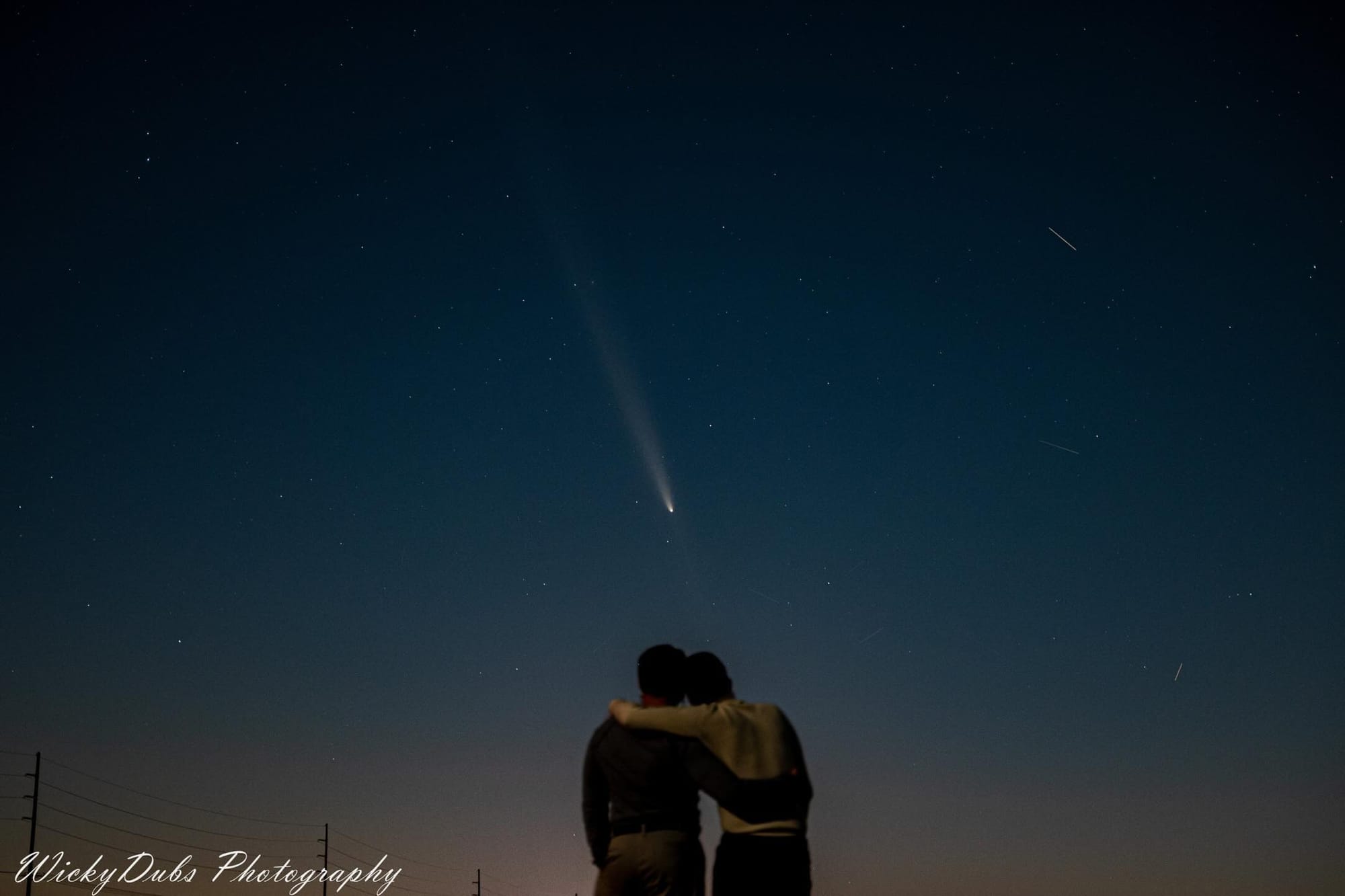 Two men embrace and look up to a comet in the nights sky.