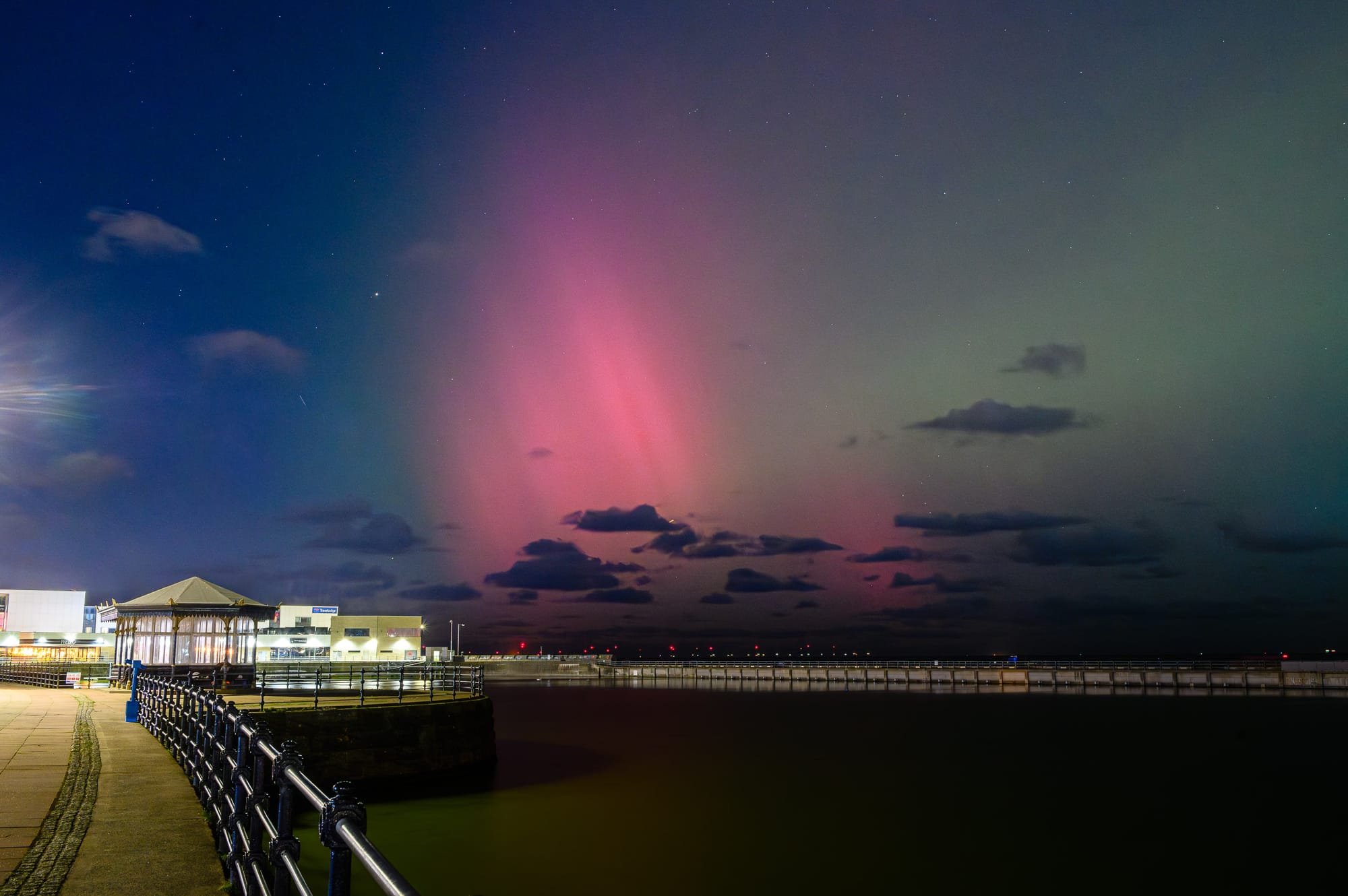 A purple flare from an aurora floats in a green sky above a marine lake.