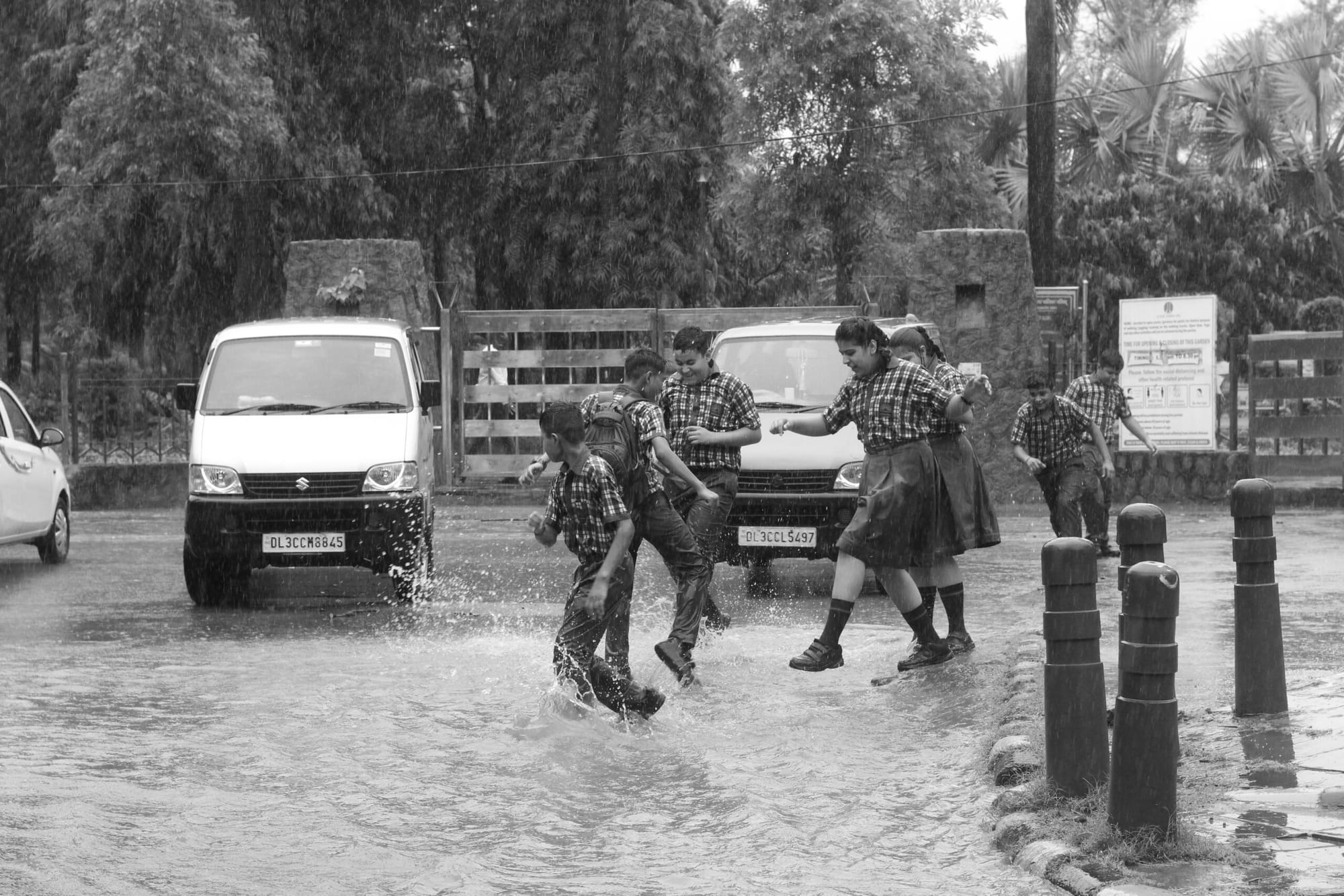 A group of school kids splash about in a large puddle on a rainy day.