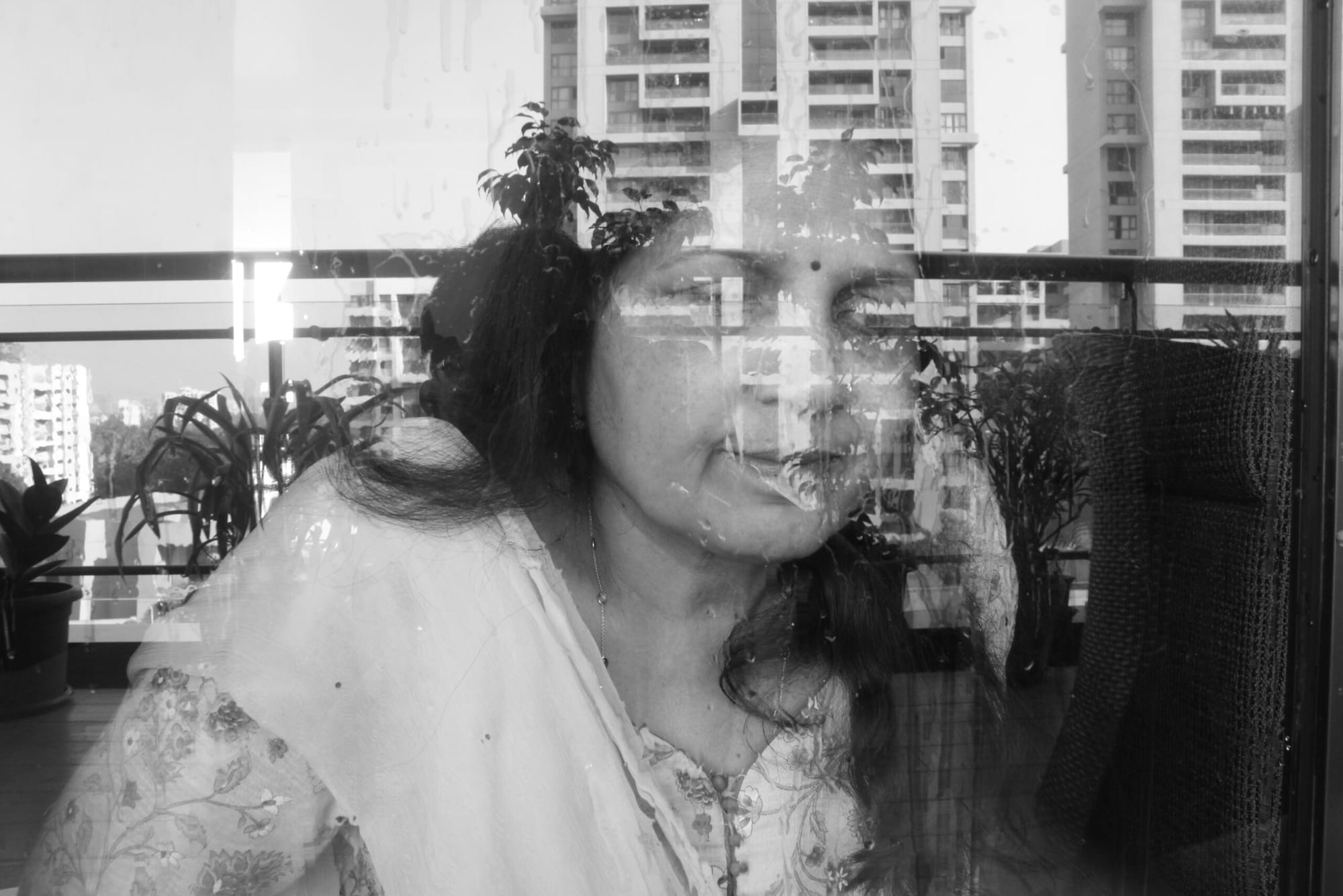 A woman looks out a window while the skyline of the city is reflected in it.