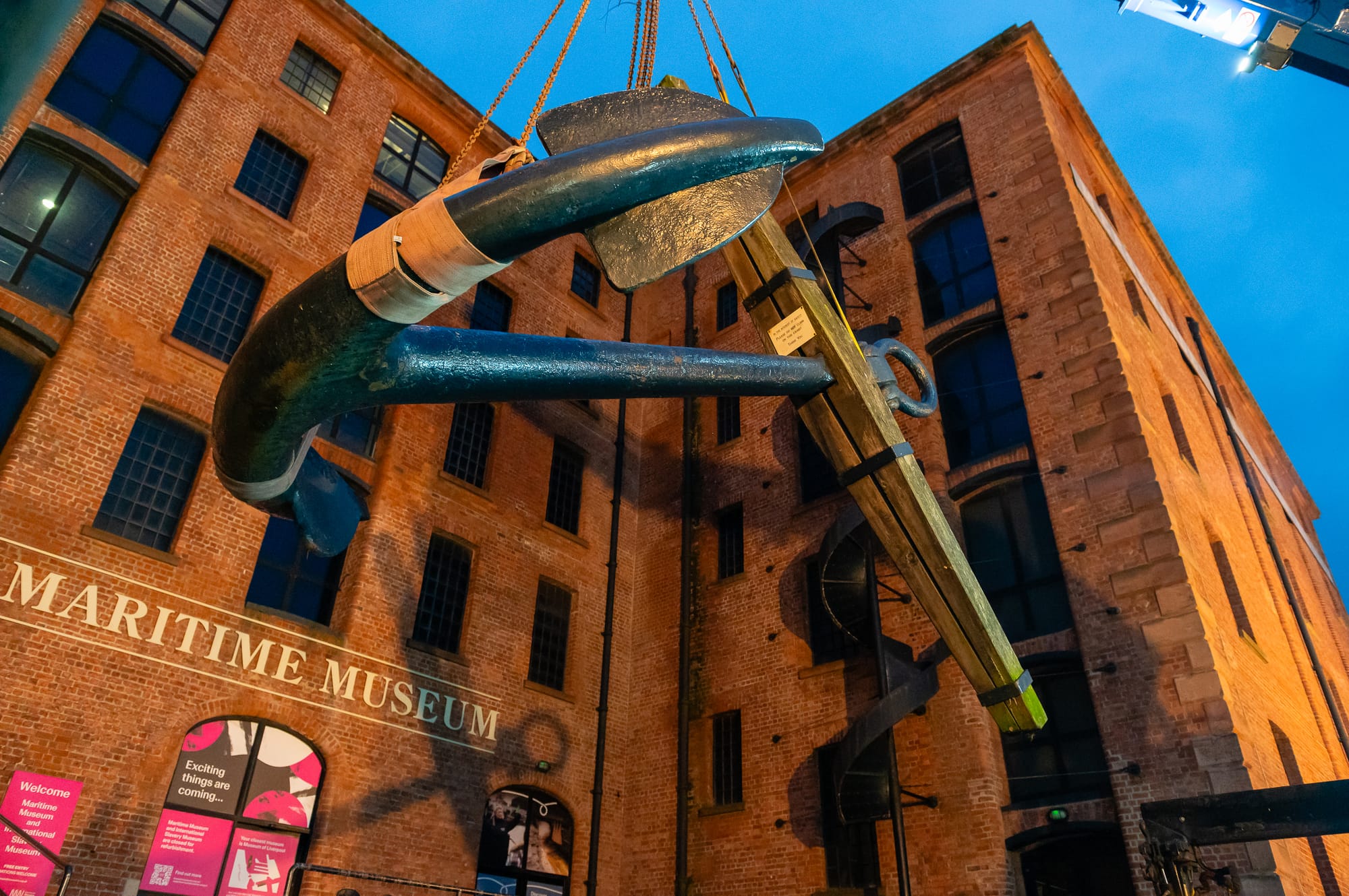 A large anchor is being lifted by a crane in front of the Maritime Museum in Liverpool.