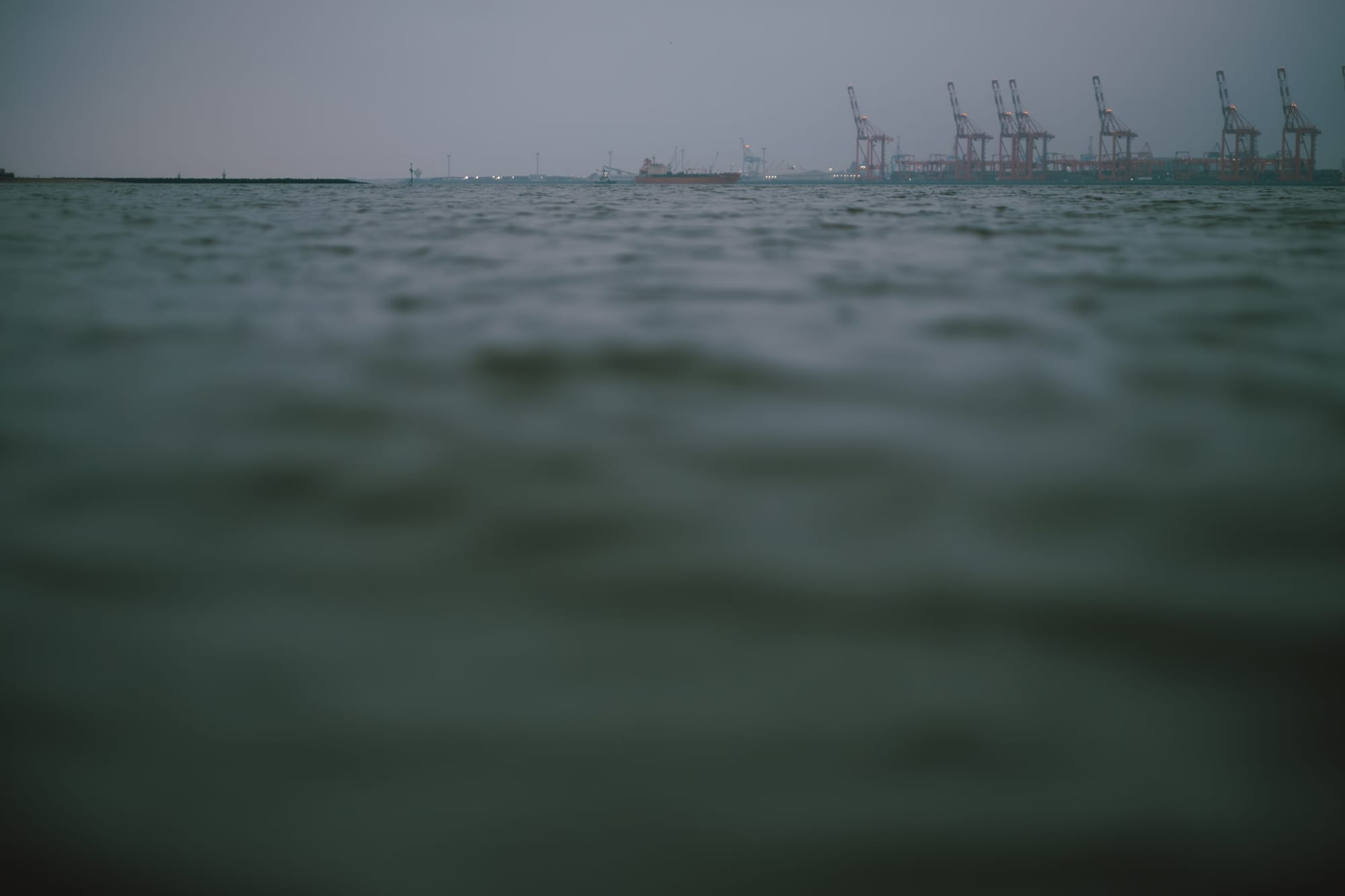 A blurry image of the Mersey River with container cranes in the distance.