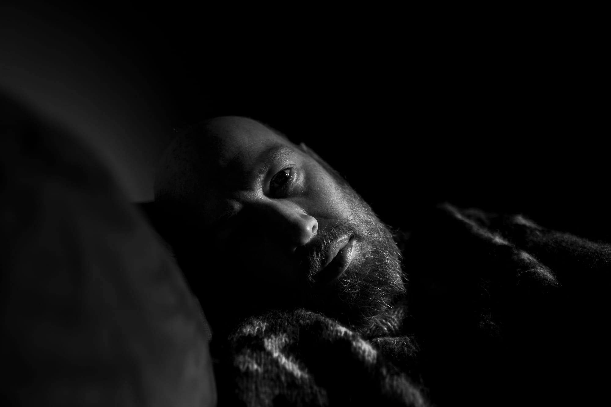 Black and white photo of a man lying down and looking at the camera.